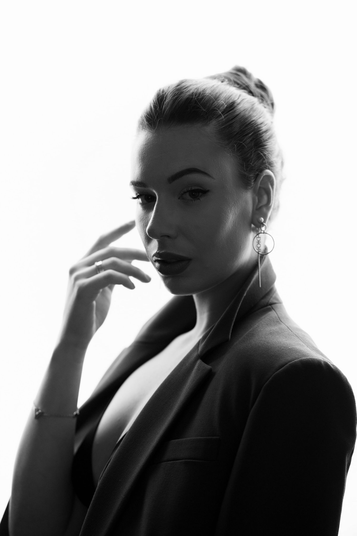 Black and white portrait of an elegant woman in a blazer with hair up, touching her face.