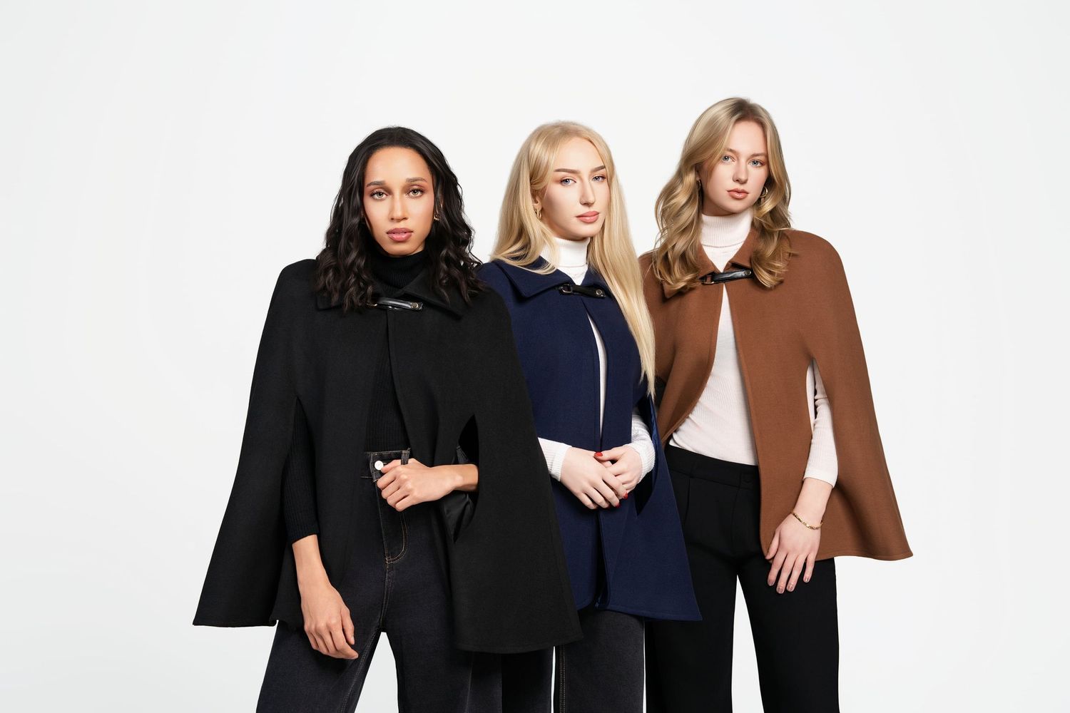 Three women modeling stylish cape coats in black, navy, and camel on a white background.