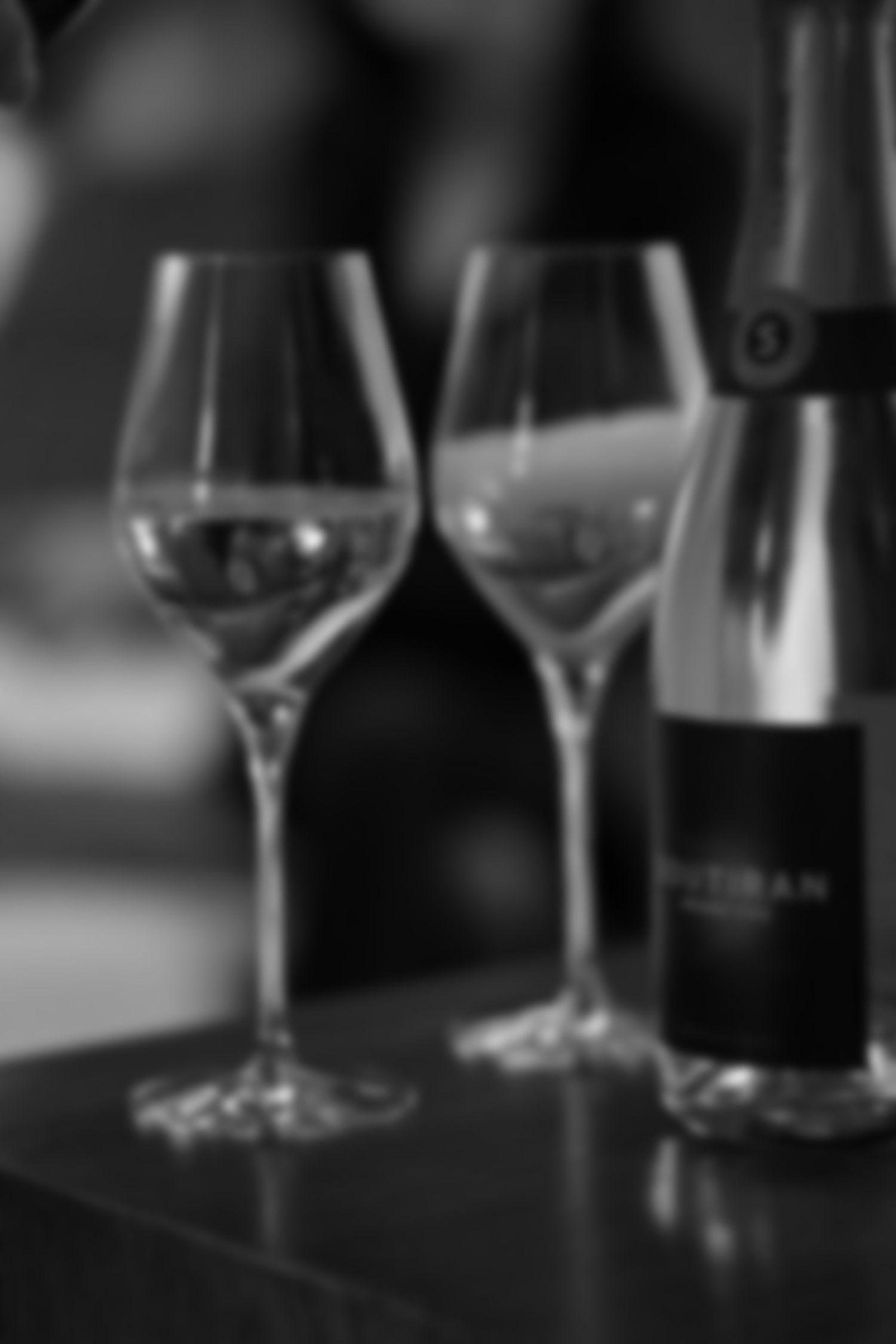 Soft focus black and white image of two champagne flutes beside a Soutiran bottle.