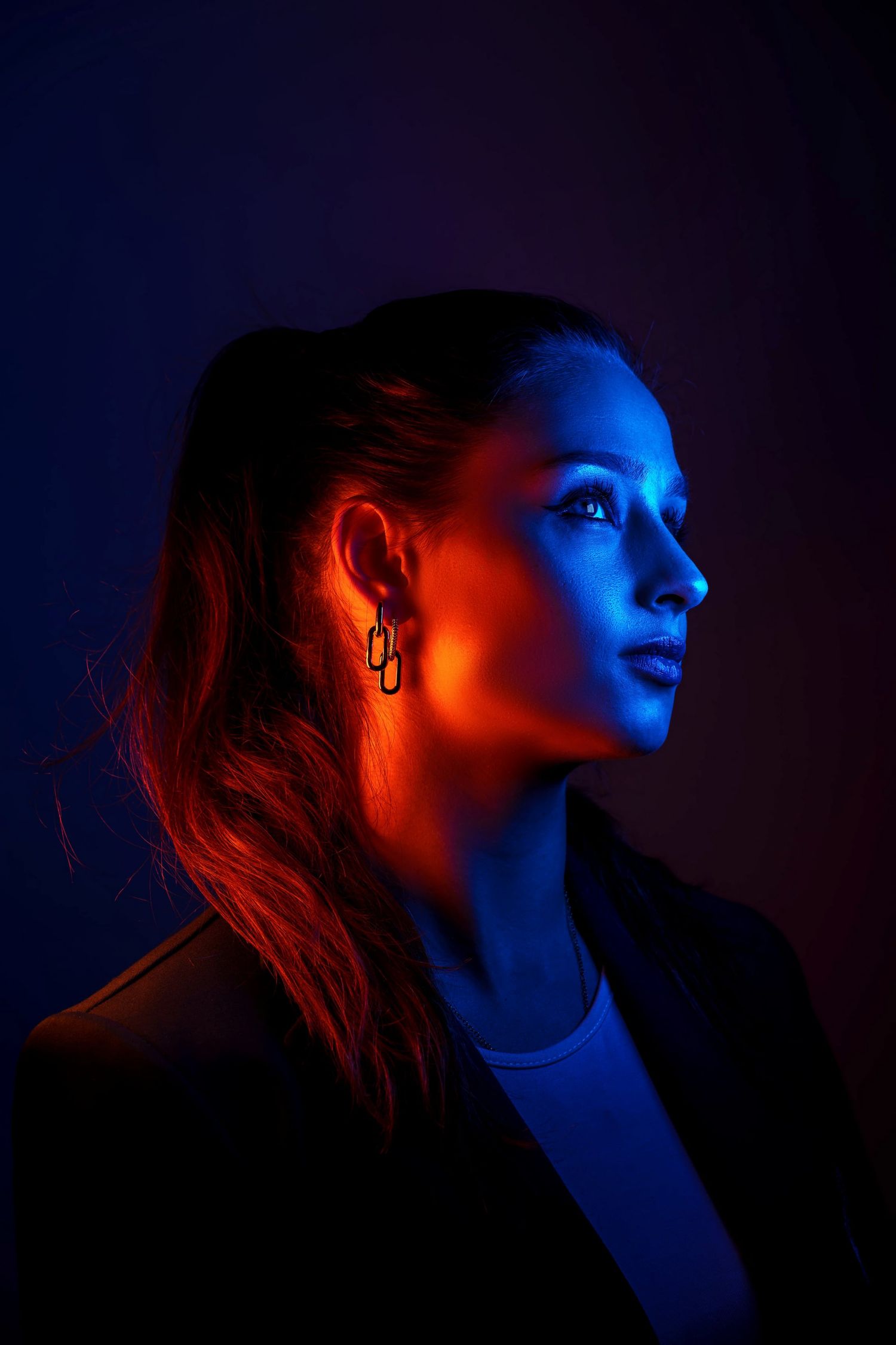 Woman in profile illuminated by dramatic red and blue neon lights against a dark background.