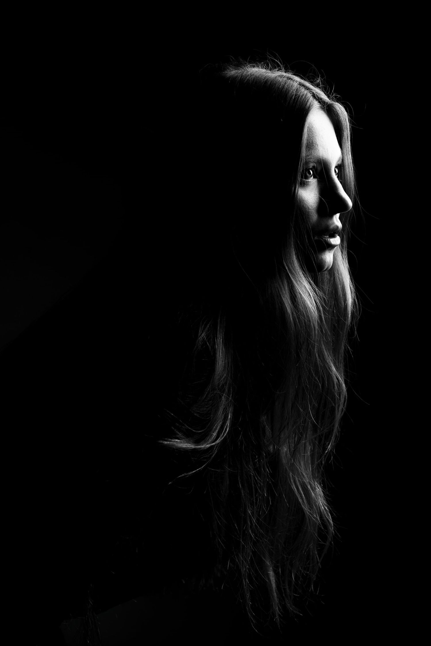 Dramatic black and white low-key portrait of woman with long hair against dark background.