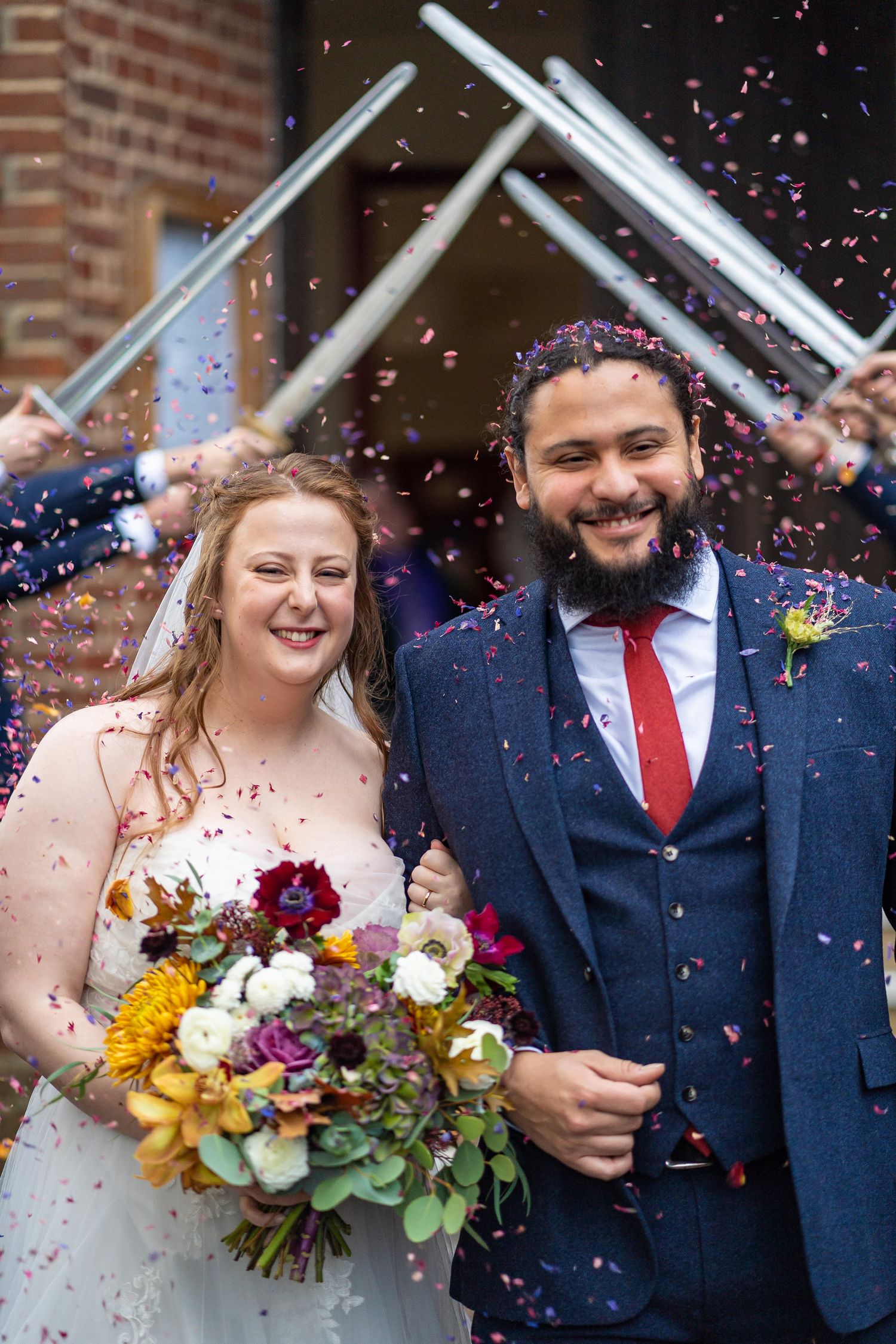 Joyful bride and groom walking through colorful confetti shower outside a brick church ceremony.