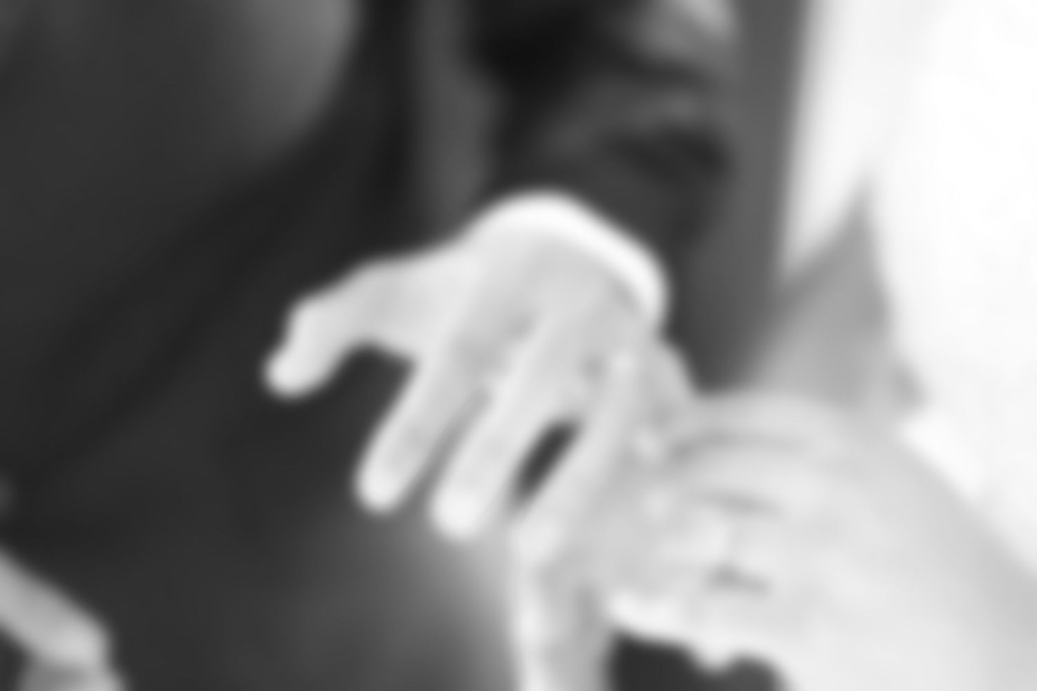 Close-up black and white photo of a newborn baby grasping an adult finger.