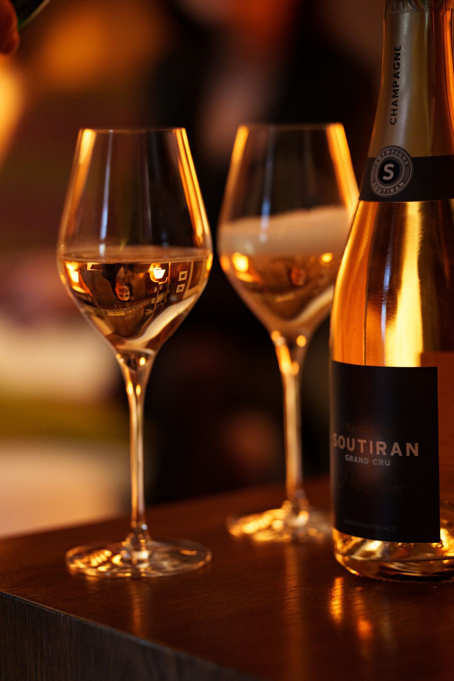 Two elegant champagne flutes being filled with Soutiran Grand Cru champagne in warm golden ambient lighting.