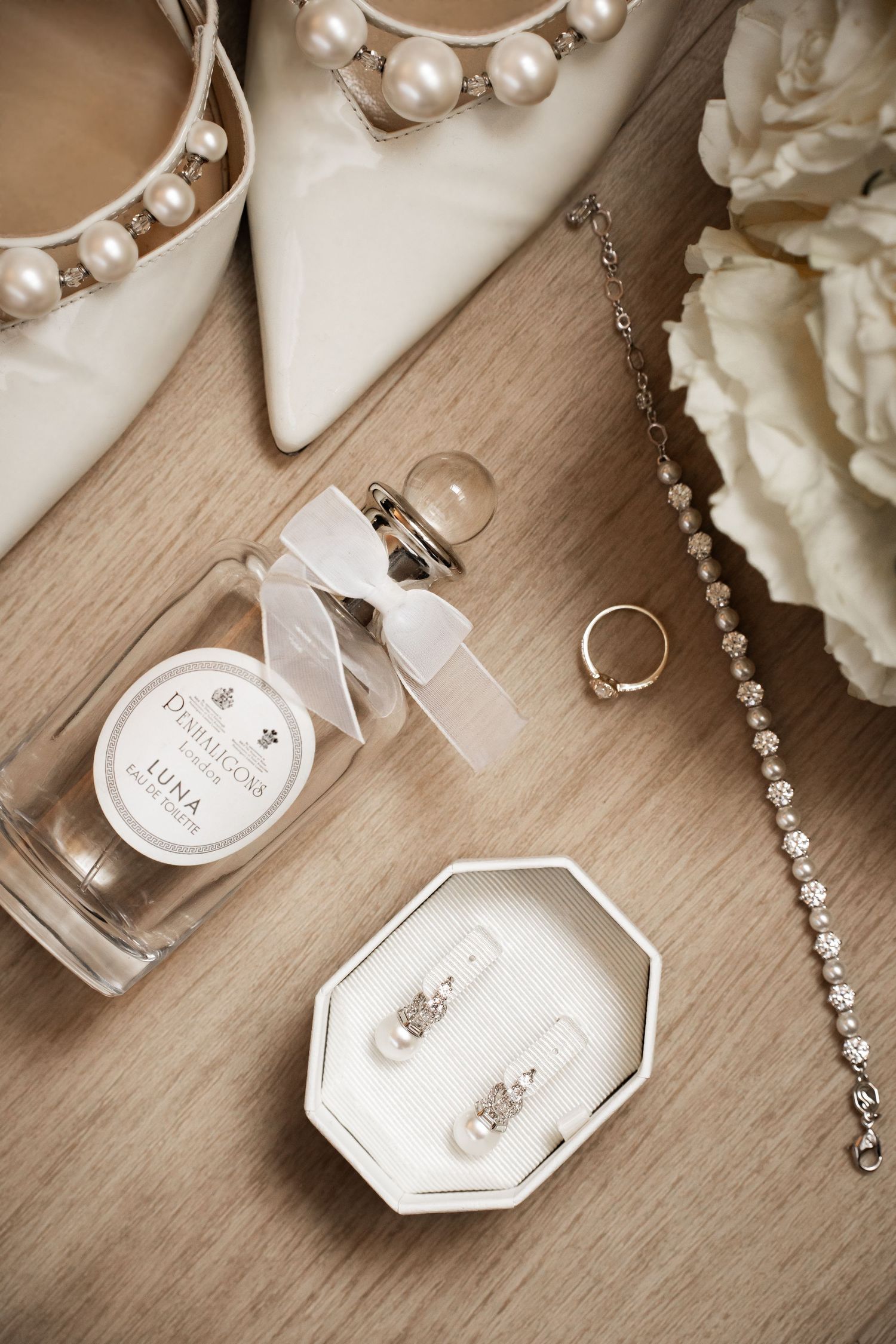 Flat lay of bridal accessories including heels, perfume, earrings, and jewelry.