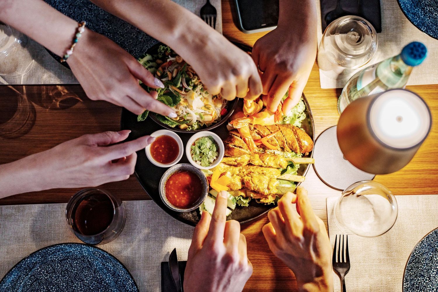 Overhead view of friends sharing appetizers with dipping sauces and beer on a wooden table.