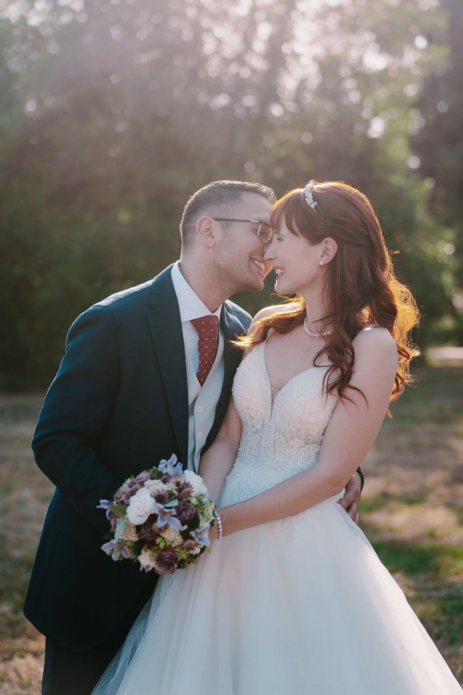 Bride and groom share a romantic almost-kiss moment outdoors in golden sunlight on their wedding day.