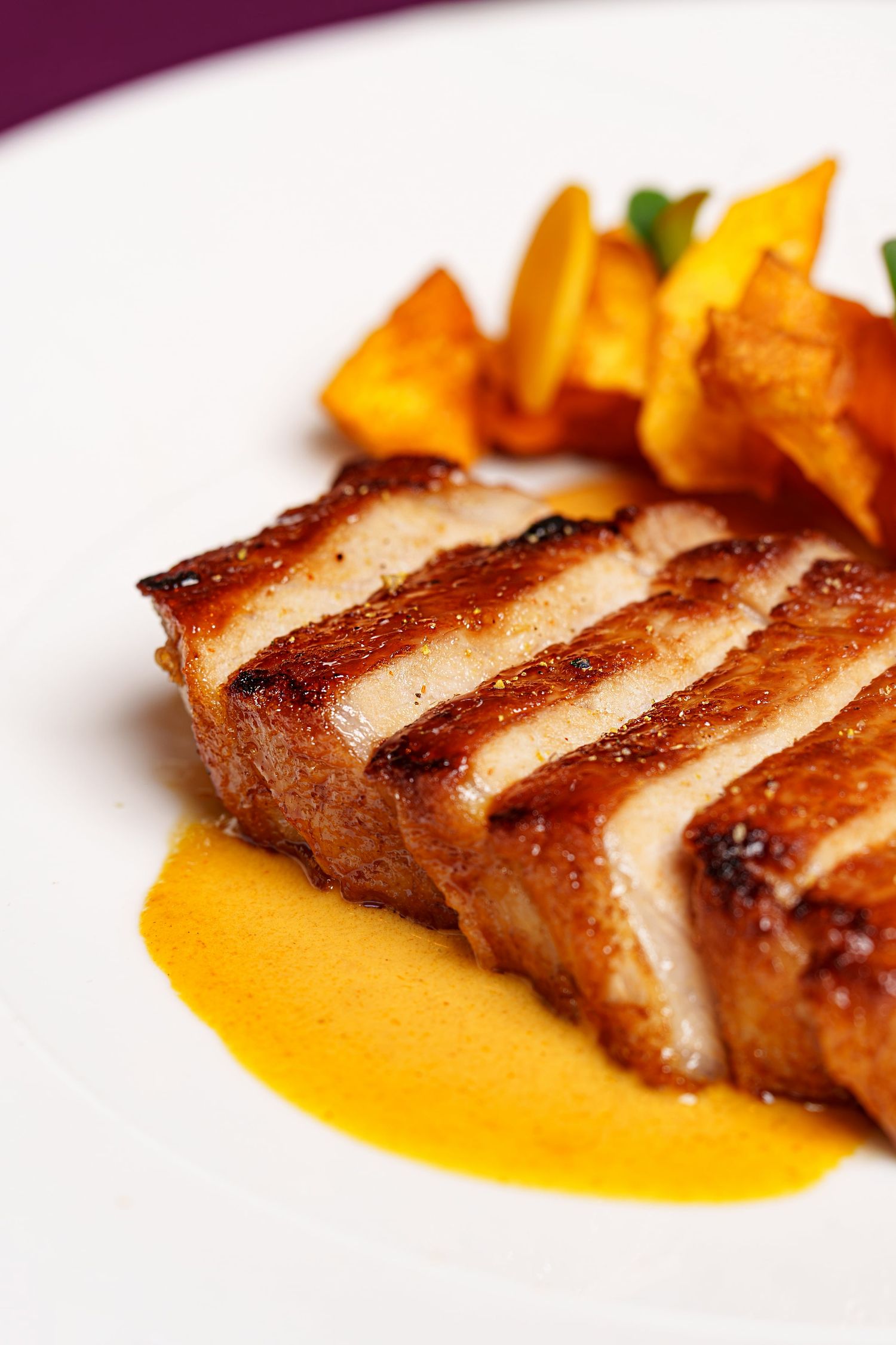 A perfectly grilled pork belly steak served with golden roasted pumpkin and orange sauce on white plate.