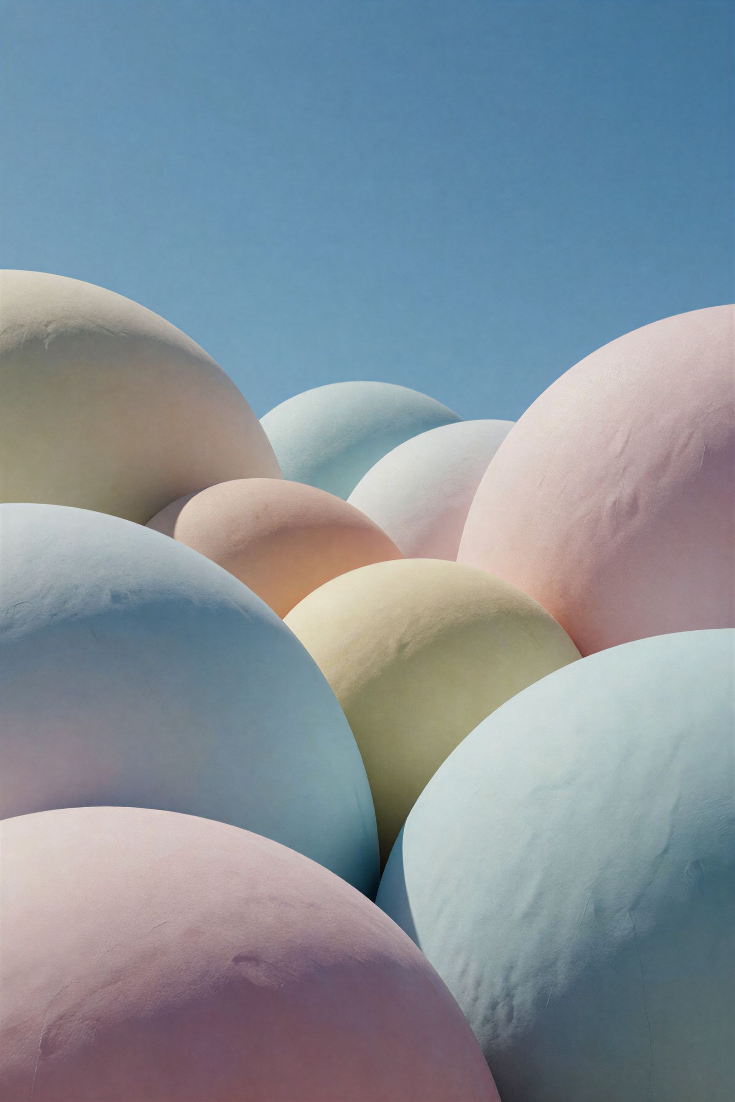 Close-up of large pastel-colored spheres in pink, blue, yellow, and green against a clear blue sky.
