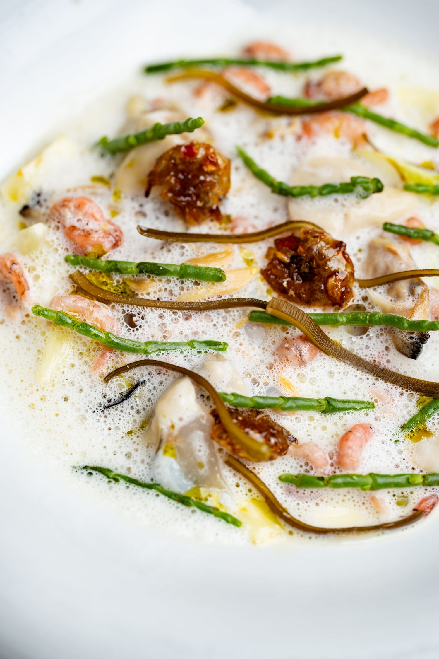 Elegant seafood dish with foam sauce, green beans, shrimp, and caramelized figs on a white plate.