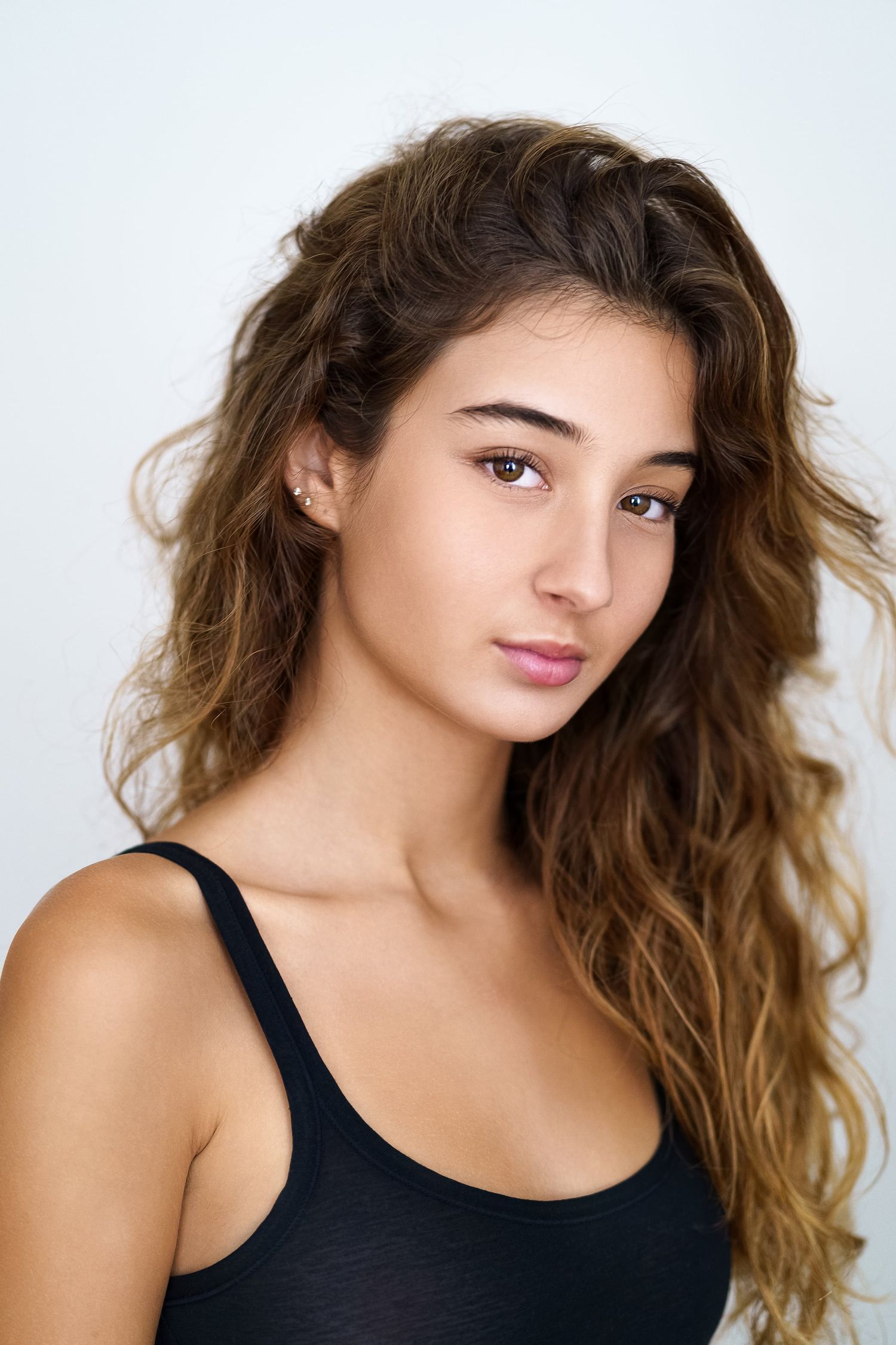 Young brunette woman with curly hair in black tank top against white background.