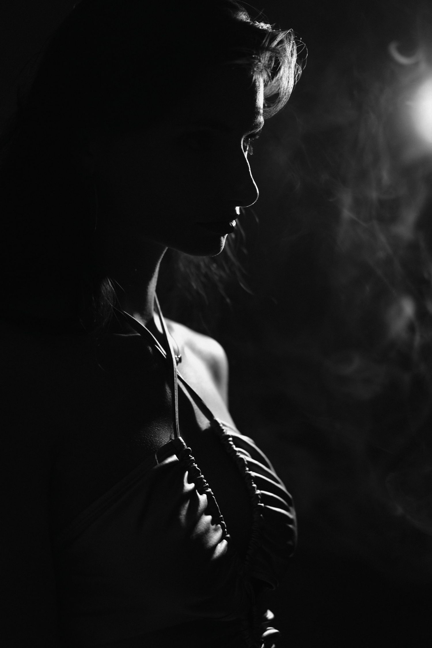 Dramatic black and white silhouette portrait of a woman with smoke in a moody low-key studio setting.