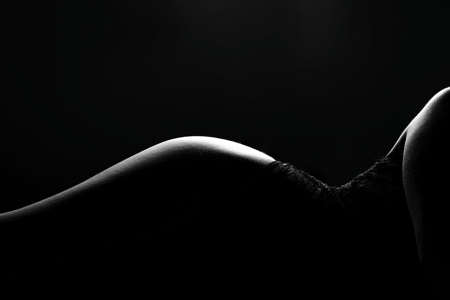 Black and white artistic silhouette of female body curves against dark background with dramatic lighting.