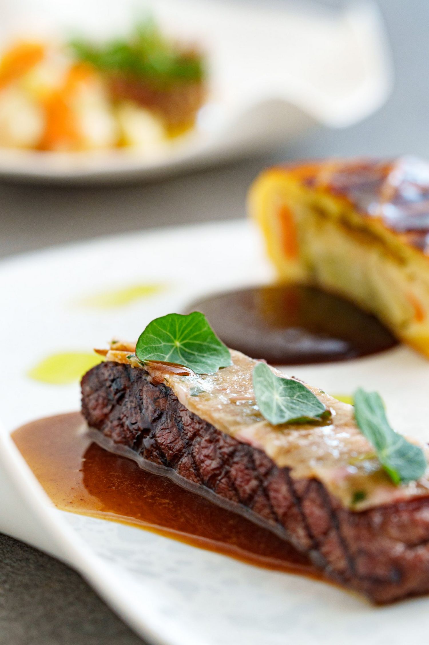 A fine dining beef dish with rich jus, fresh herb garnish, and golden gratin served on a white plate.