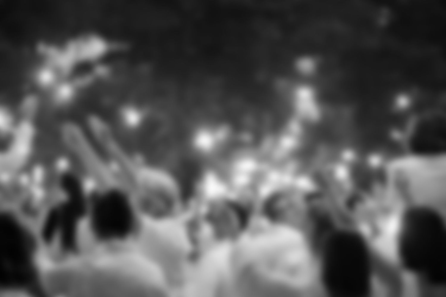 Black and white blurred photo of people in white raising sparklers at an outdoor party.