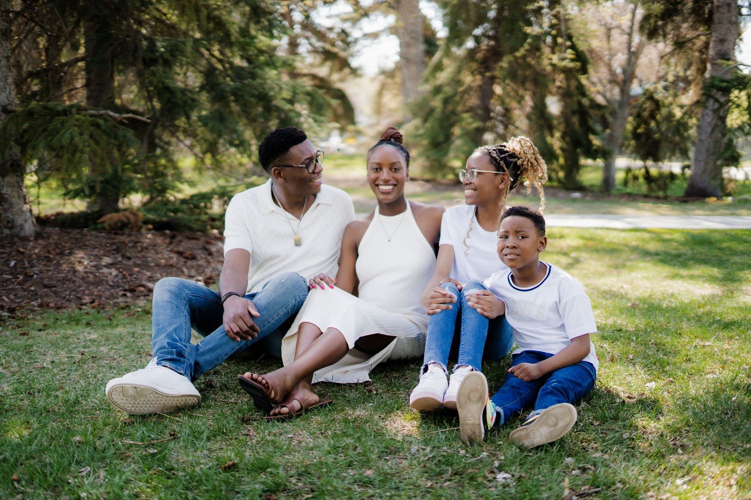 Family members relaxing on grass under trees sharing genuine laughter and embraces.