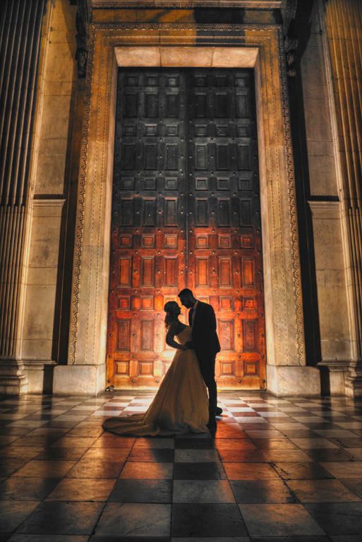 Silhouetted couple embraces in front of ornate wooden door with dramatic lighting.