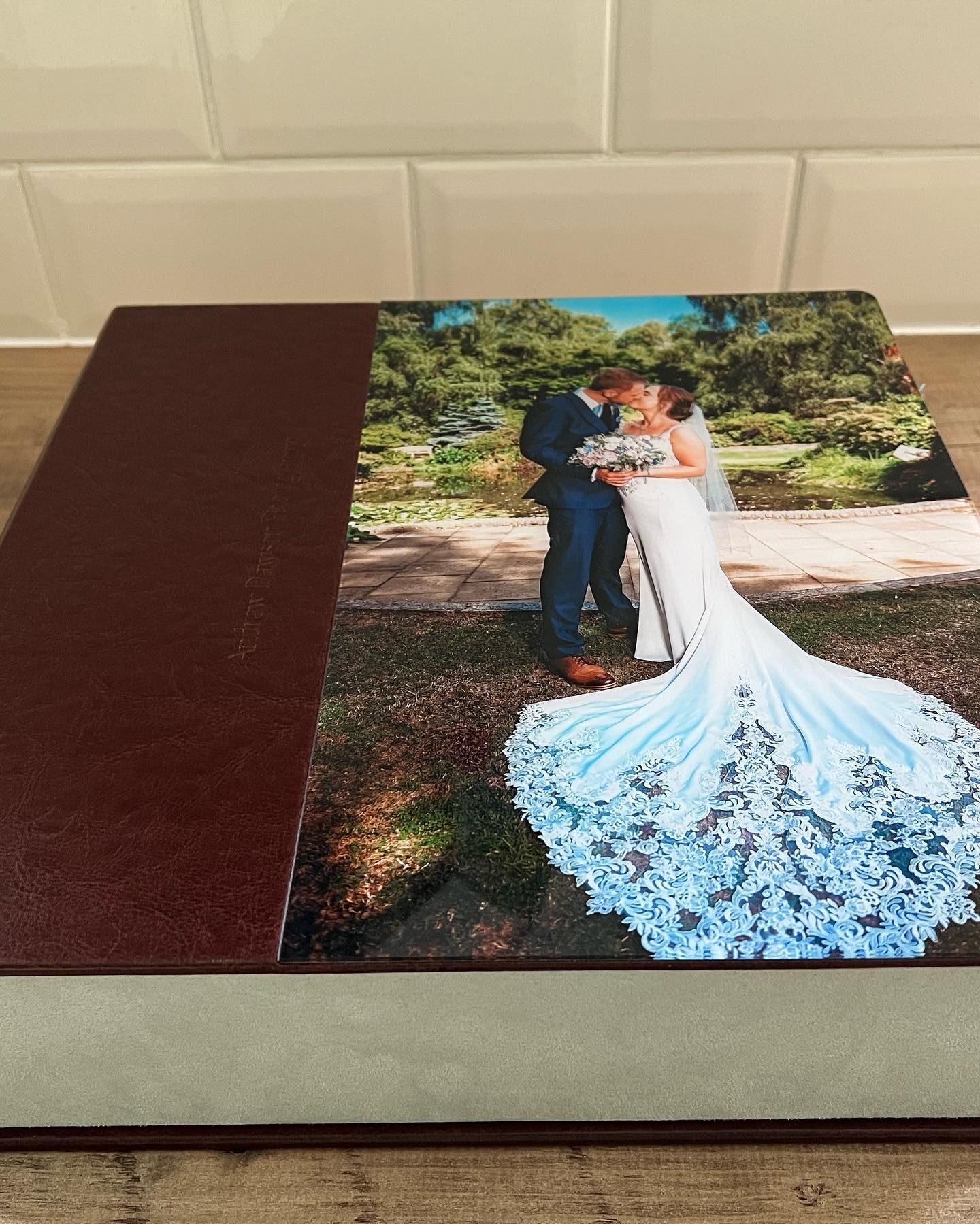 A wedding album displays a photo of a bride in a lace train gown with her groom in a garden setting.