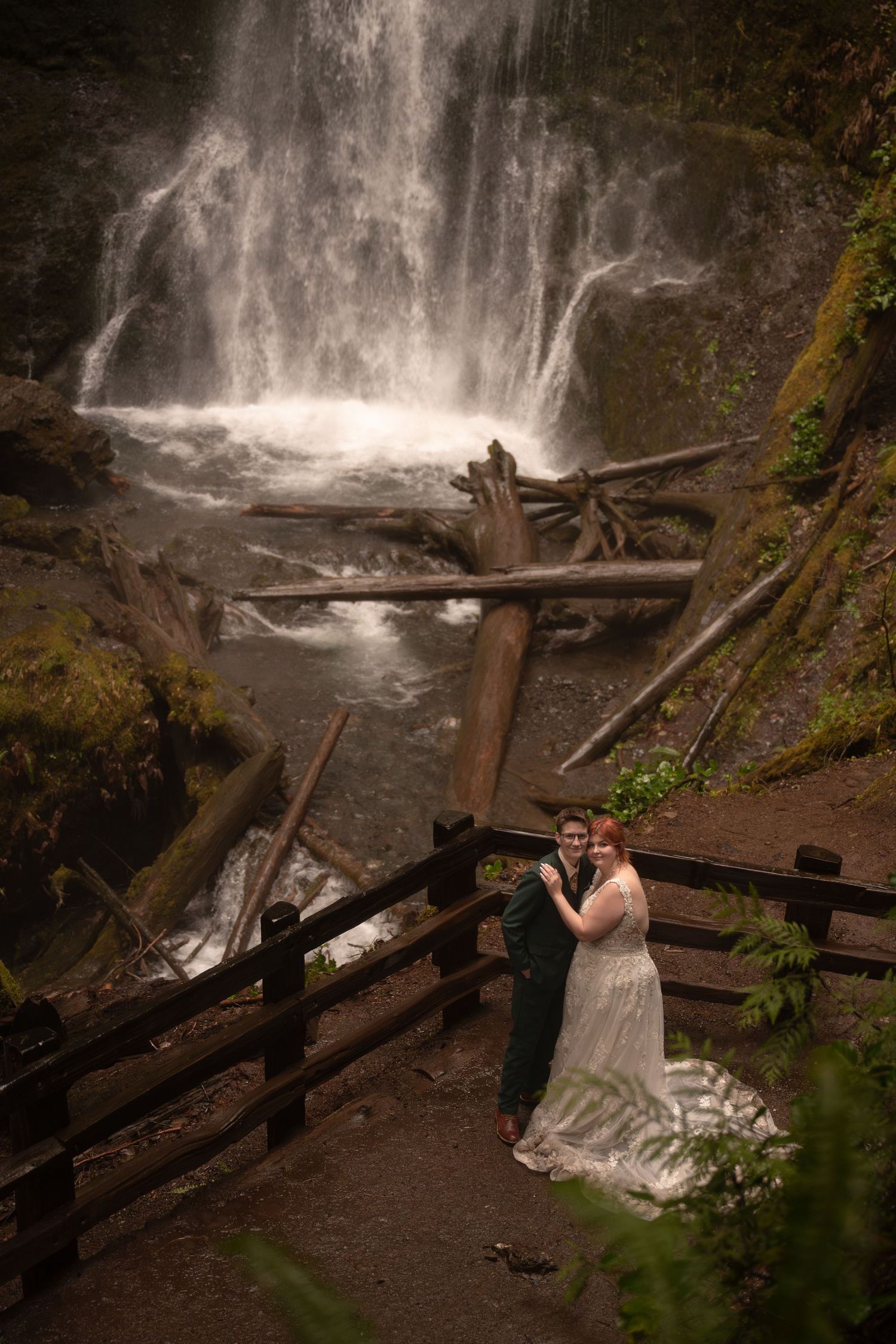 A queer couple leans against a railing to admire a waterfall during their adventure elopement.