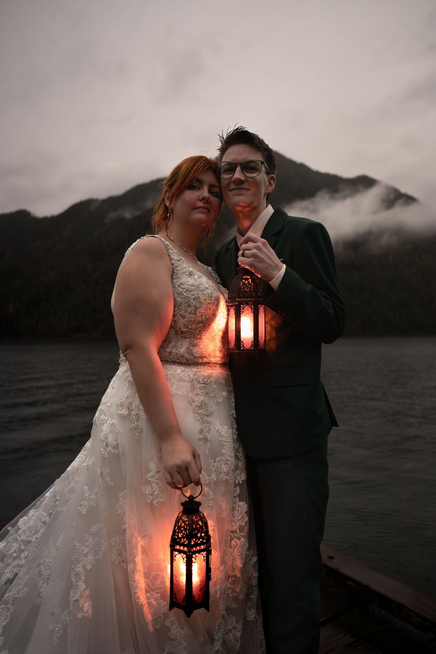 Two women embrace holding lanterns a dock on Lake Crescent in Olympic National Park, celebrating their Pacific Northwest adventure elopement