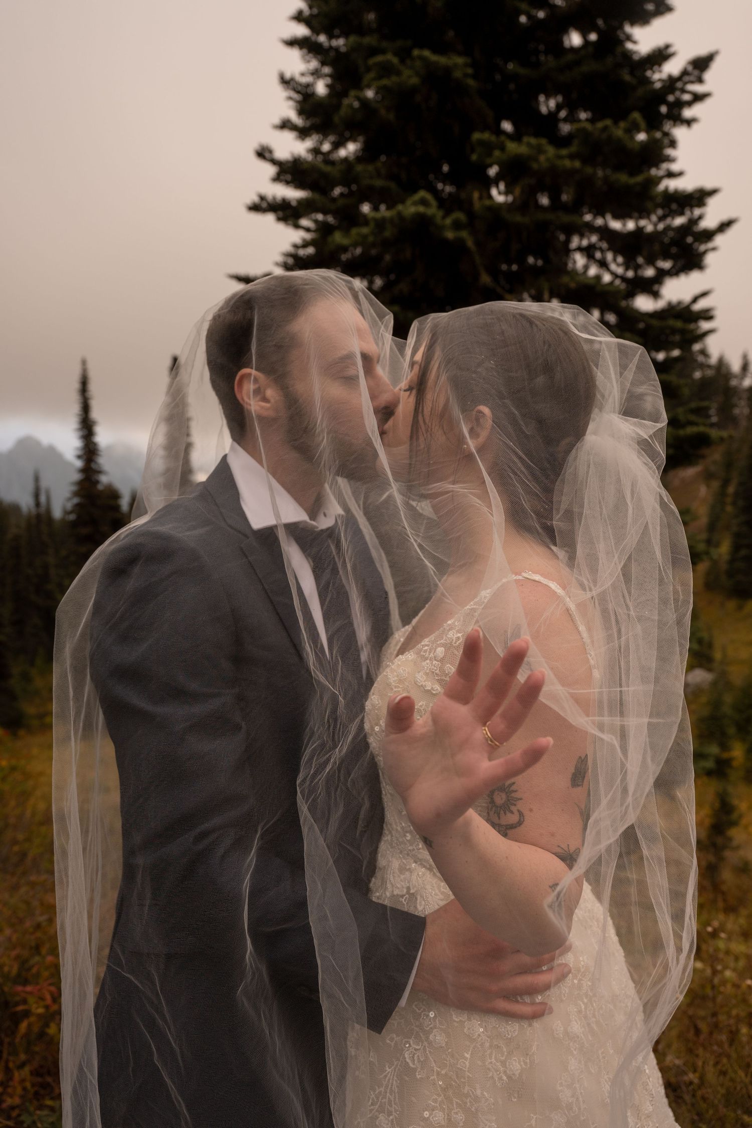 A veil conceals a couple as they share a kiss on their elopement day in the forest of the Pacific Northwest.
