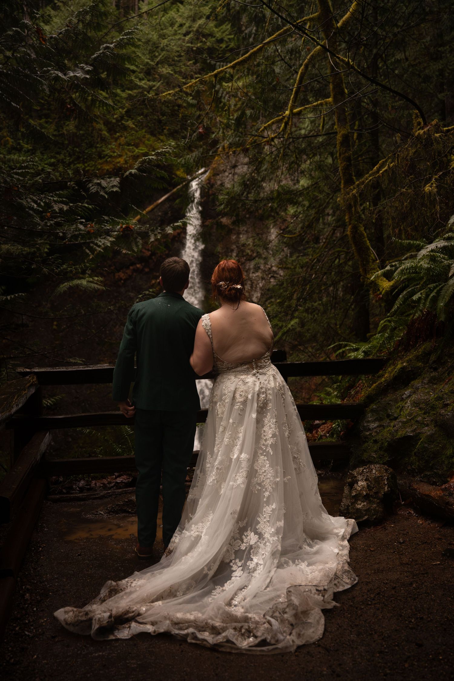 Two women embrace each other in front of Marymere Falls, celebrating their Pacific Northwest adventure elopement