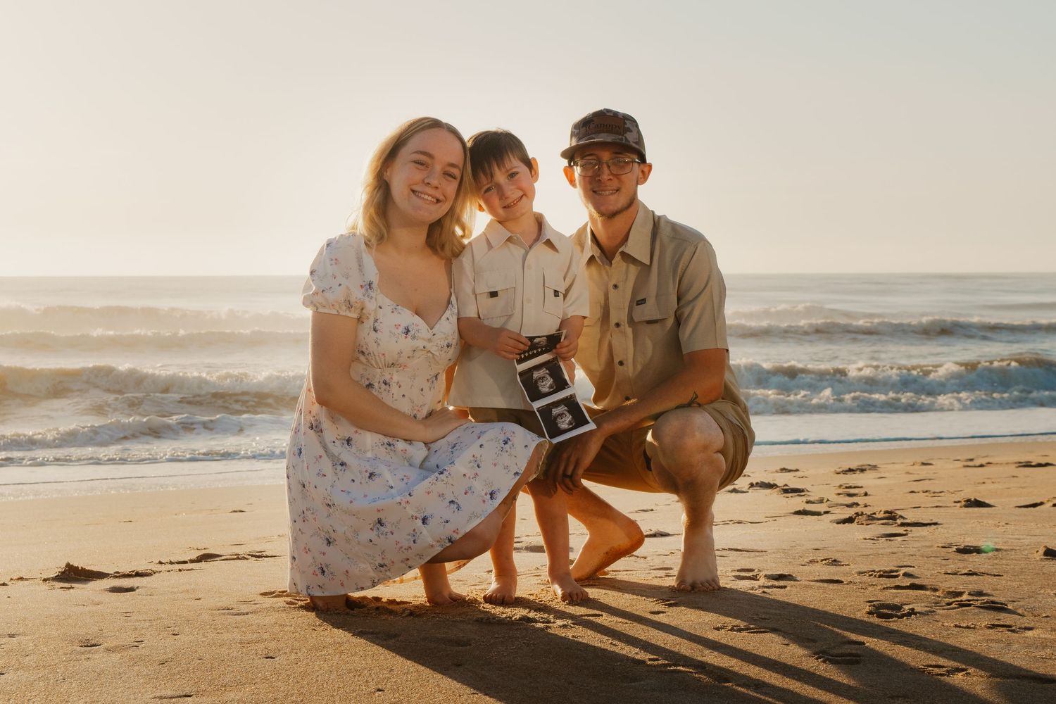 Family enjoying a sunset beach photoshoot together while sitting on sandy shore with ocean waves in background.