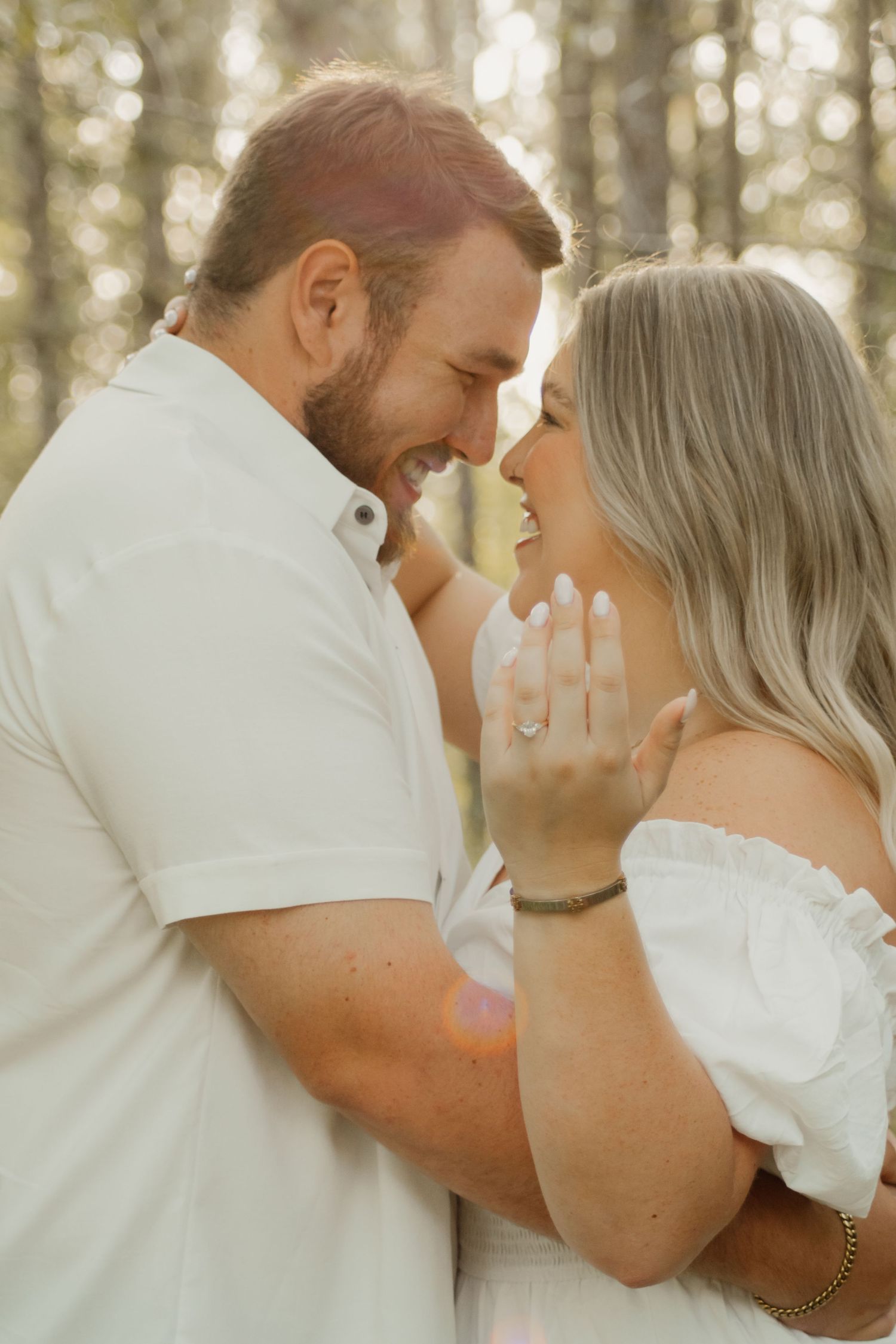 A romantic couple shares intimate moments in a sun-drenched forest setting wearing white and embracing tenderly.
