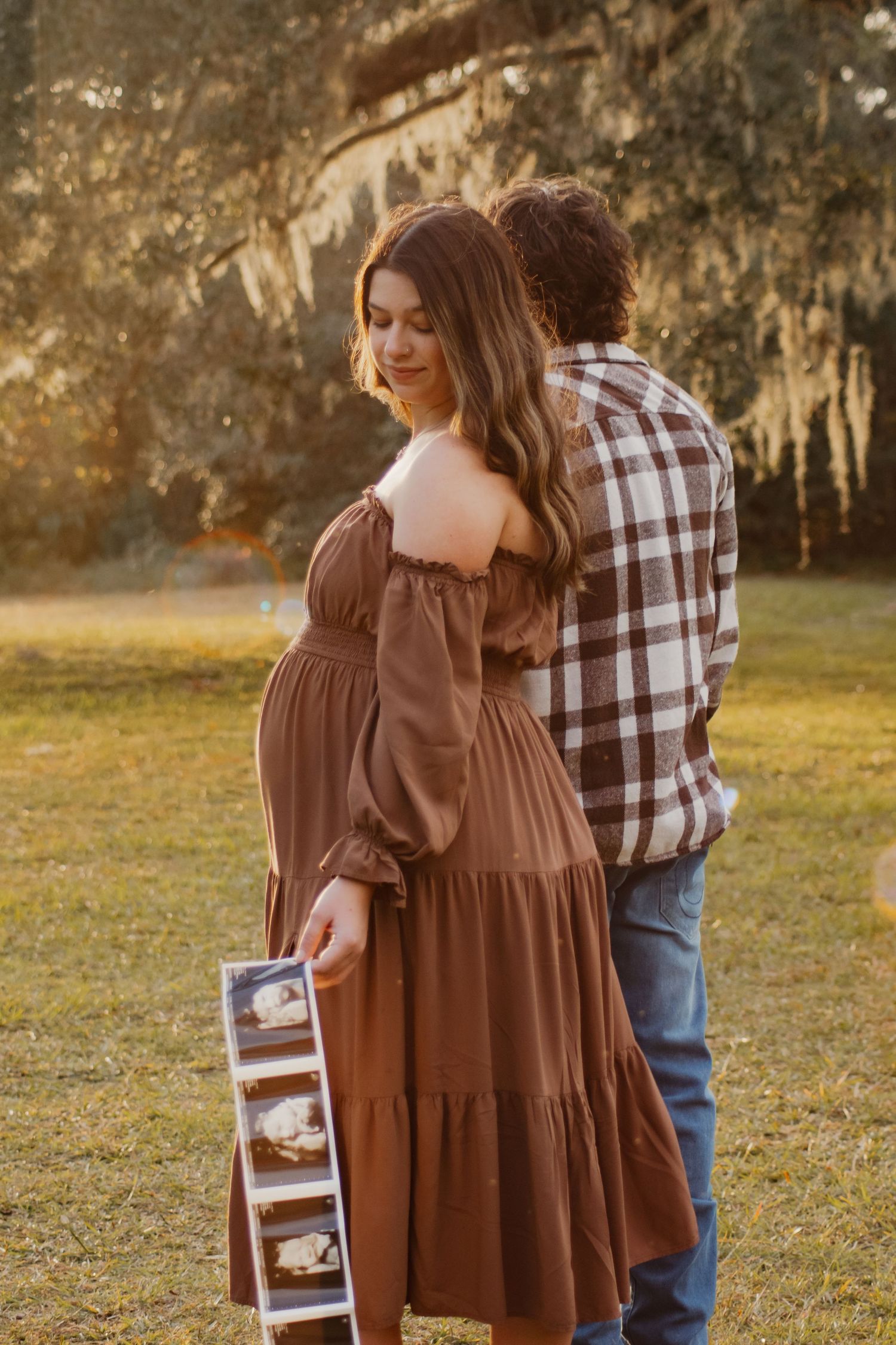 Couple in autumn setting walking outdoors while the expectant mother shows off her ultrasound picture.