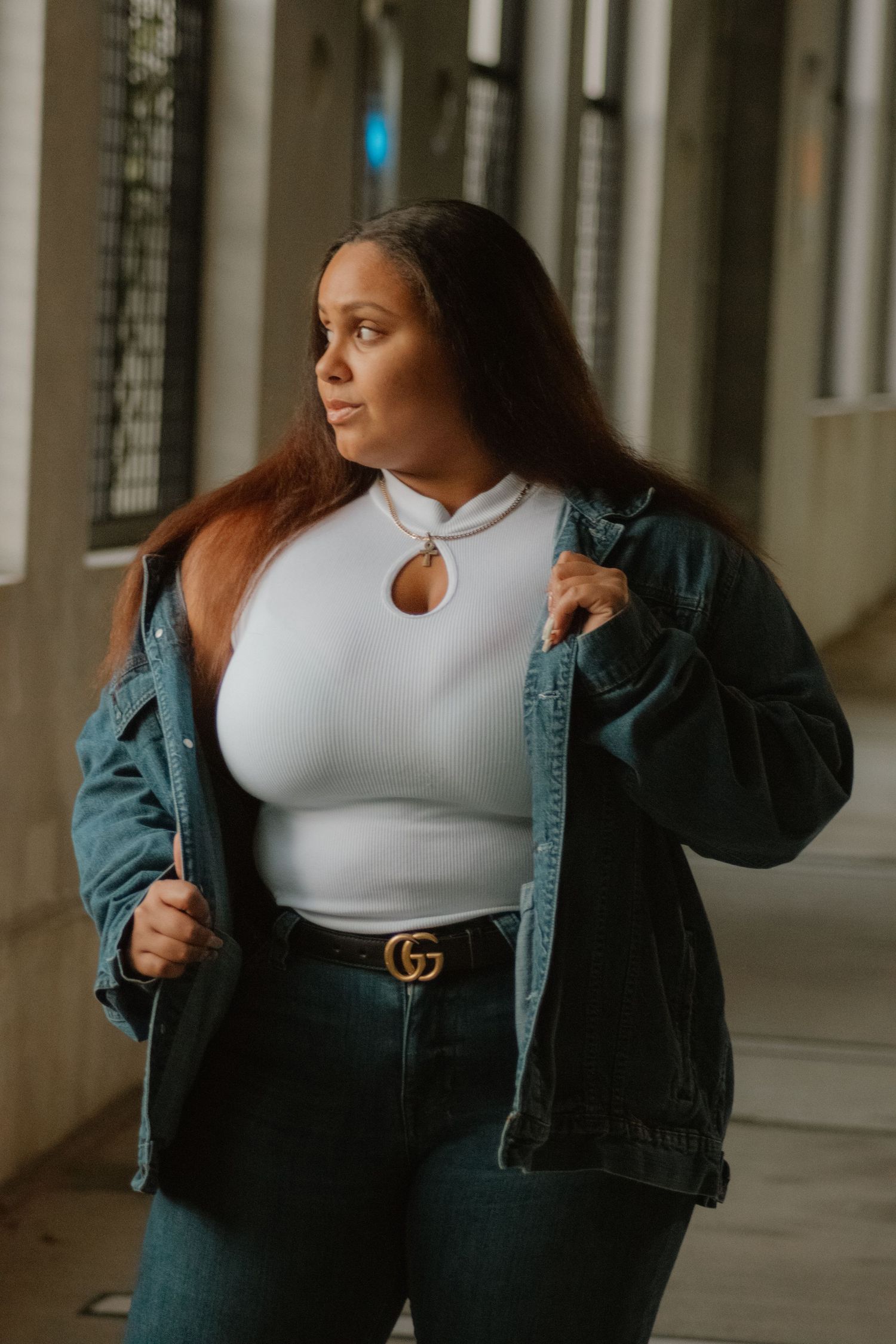 Fashion model wearing white crop top and denim jacket poses in architectural setting with natural lighting.