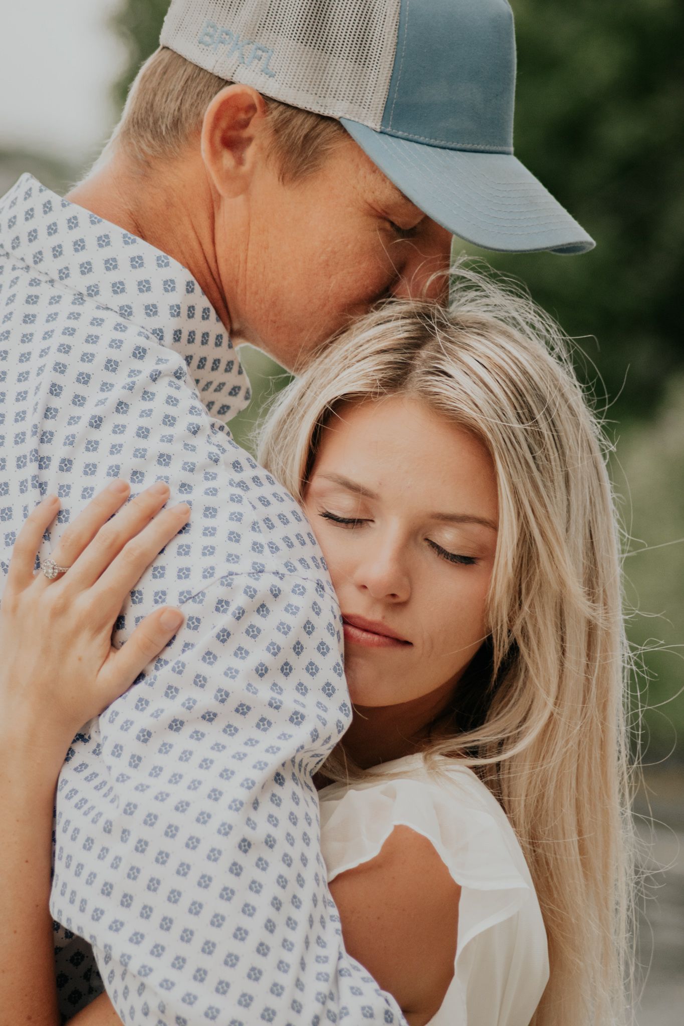 A couple embraces with their eyes closed while the woman shows off her sparkly new engagement ring.
