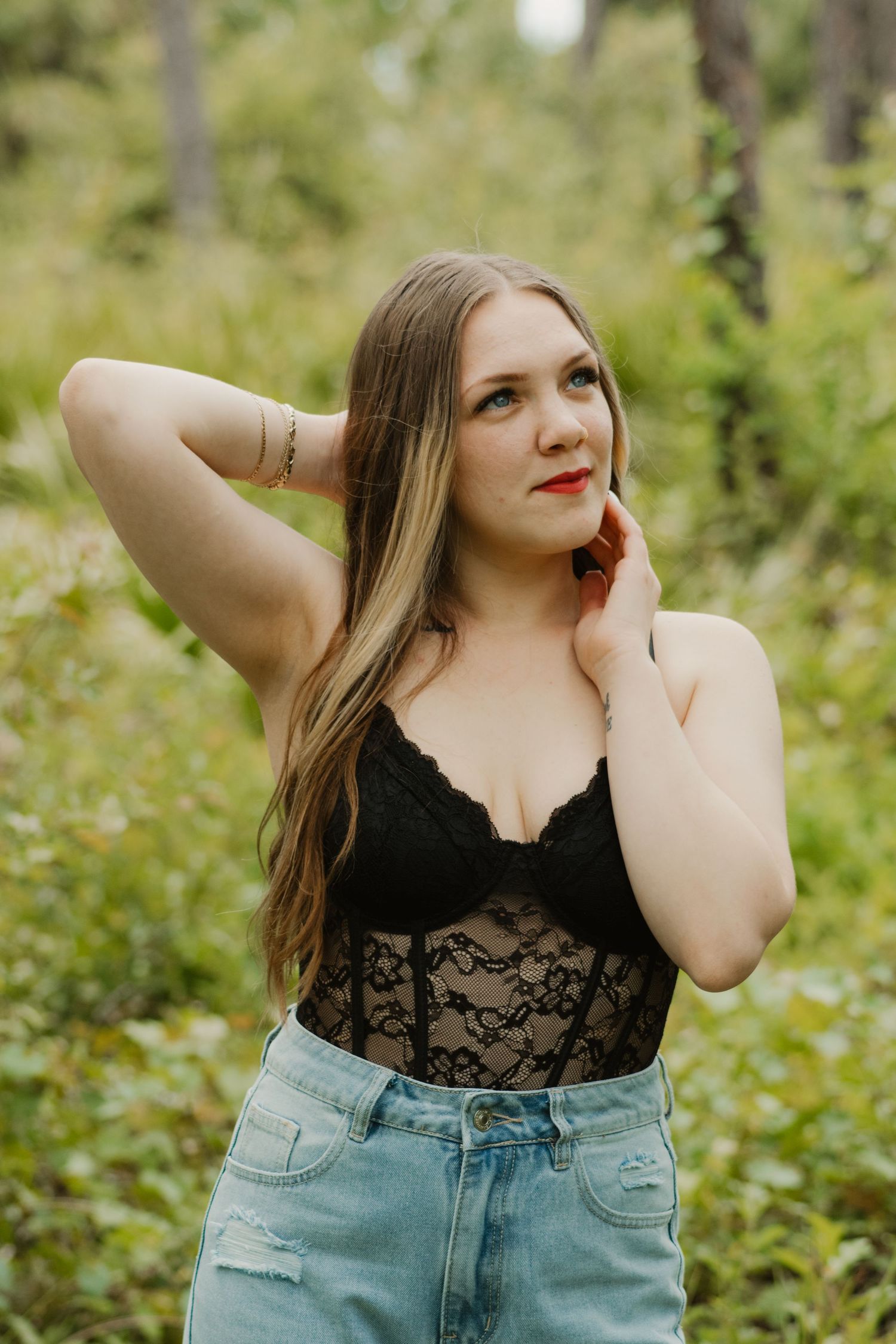 A person in a black lace top and denim jeans poses outdoors against a natural green background in multiple shots.