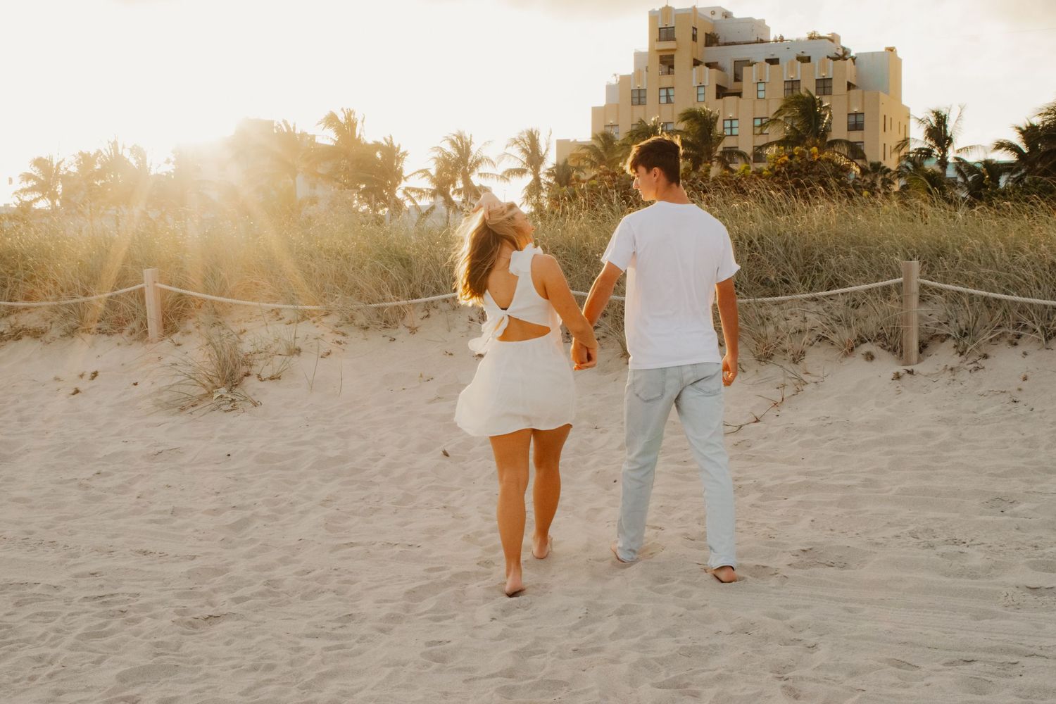A couple walks hand in hand along a sandy beach at sunset creating romantic silhouettes against the golden sky.
