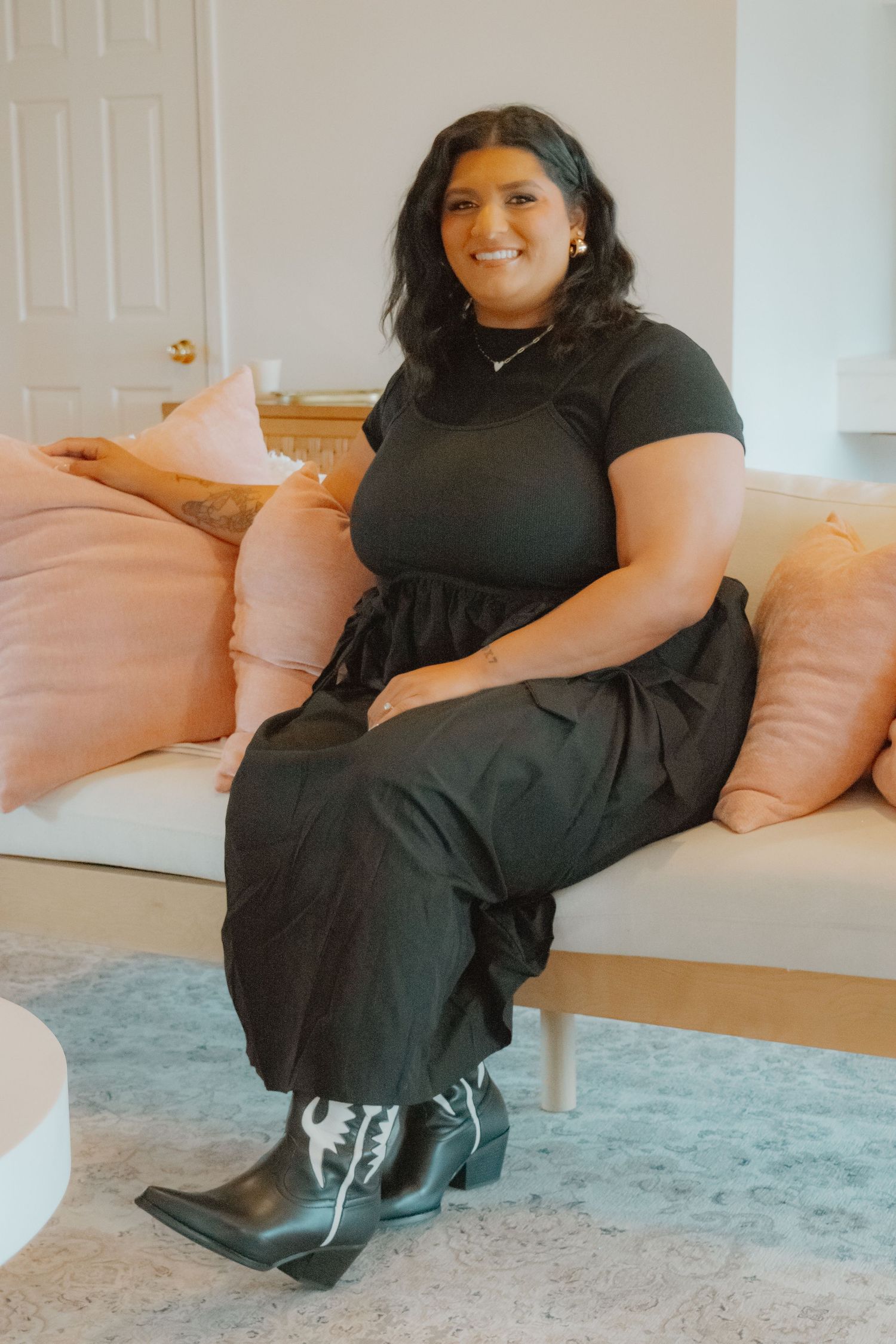 A person in a black dress sits comfortably on a light pink couch against a white wall.