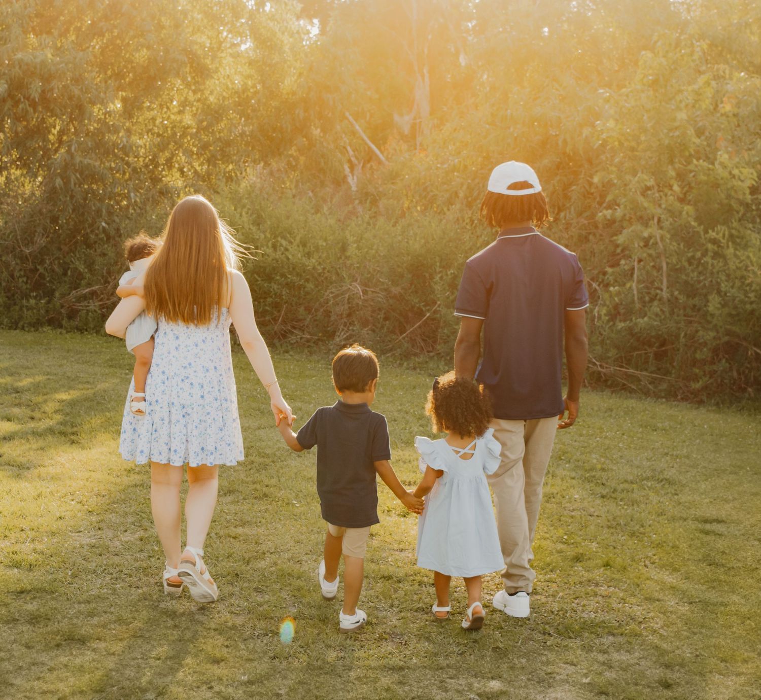A family walks together on a grassy hill during golden hour sunset, creating a warm silhouetted scene.