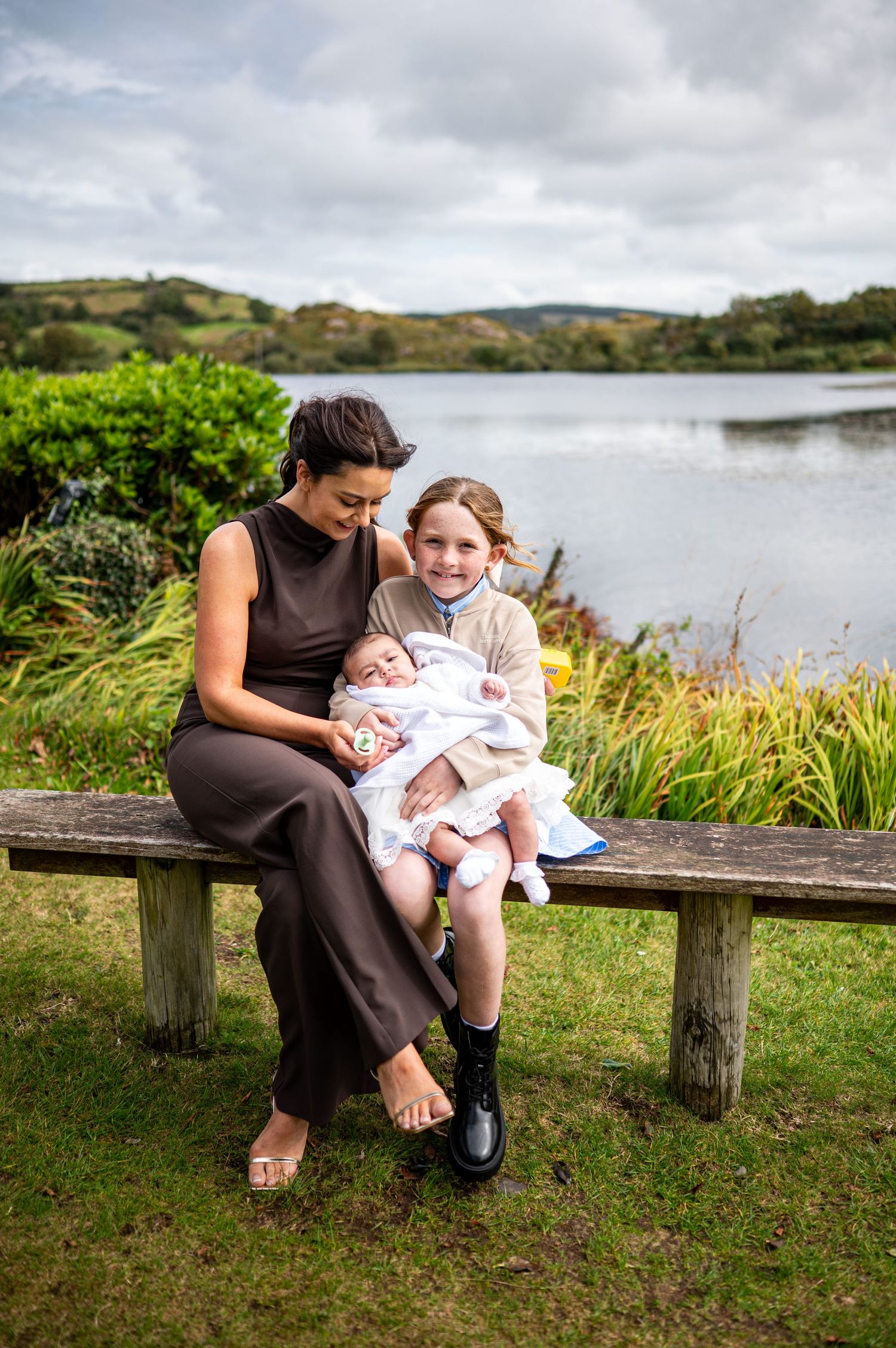 family photographer waterford christening day baby young child mam sitting by water west cork