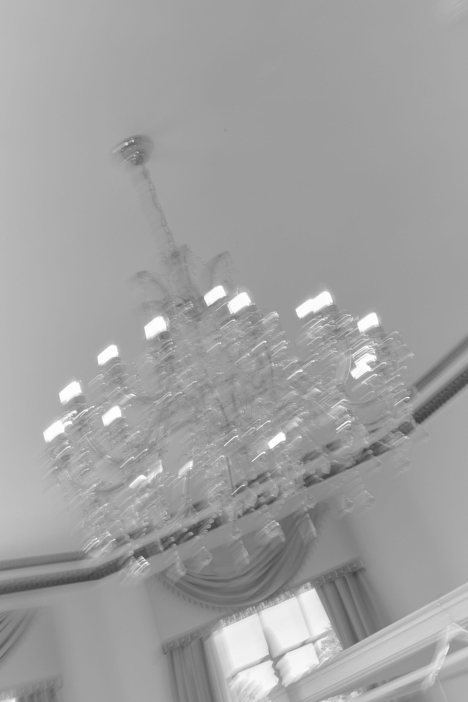 Black and white photo of an elegant crystal chandelier hanging from a ceiling, captured with motion blur effect.