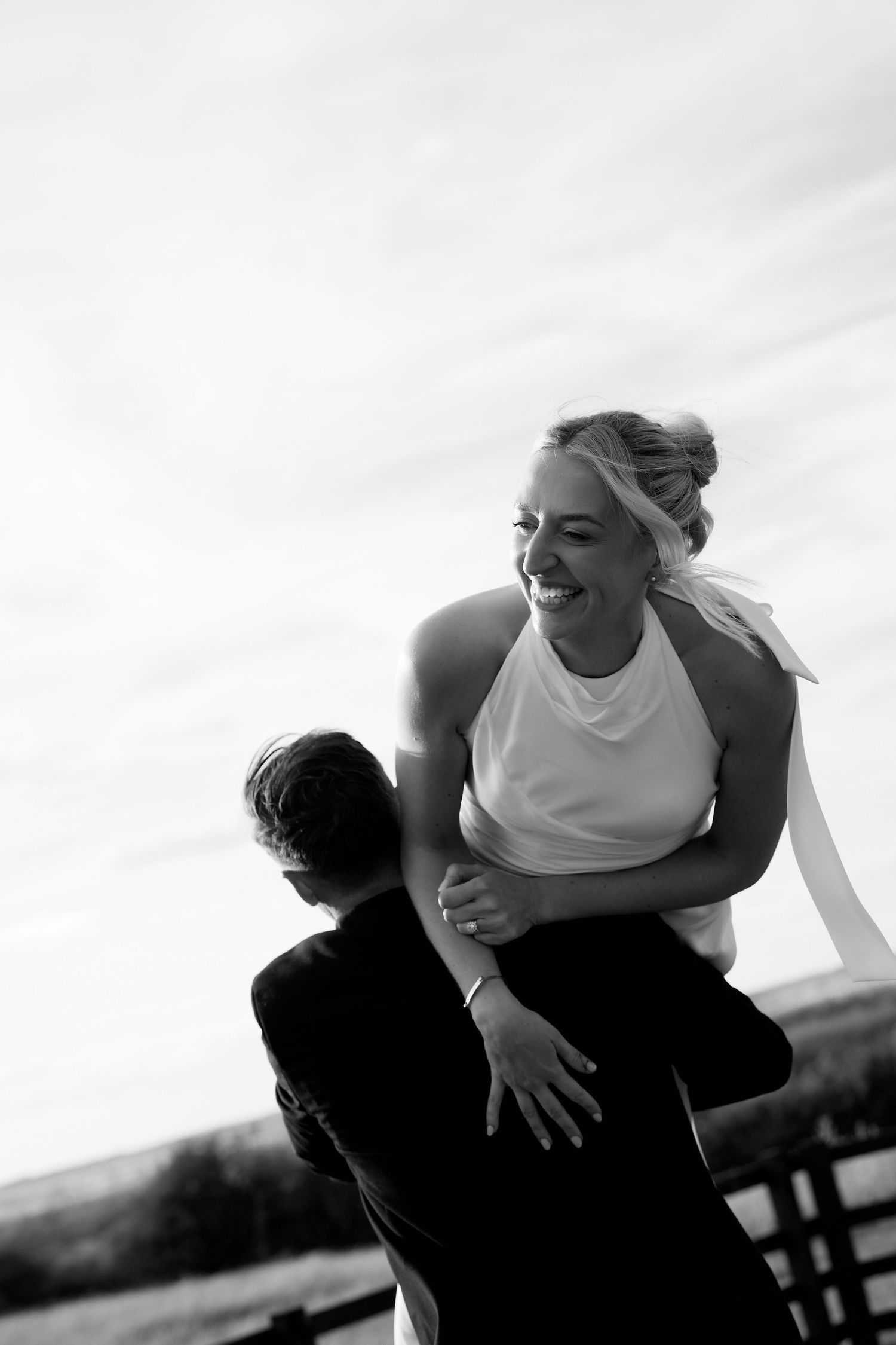 Black and white photo of a groom lifting his laughing bride outdoors on their wedding day.