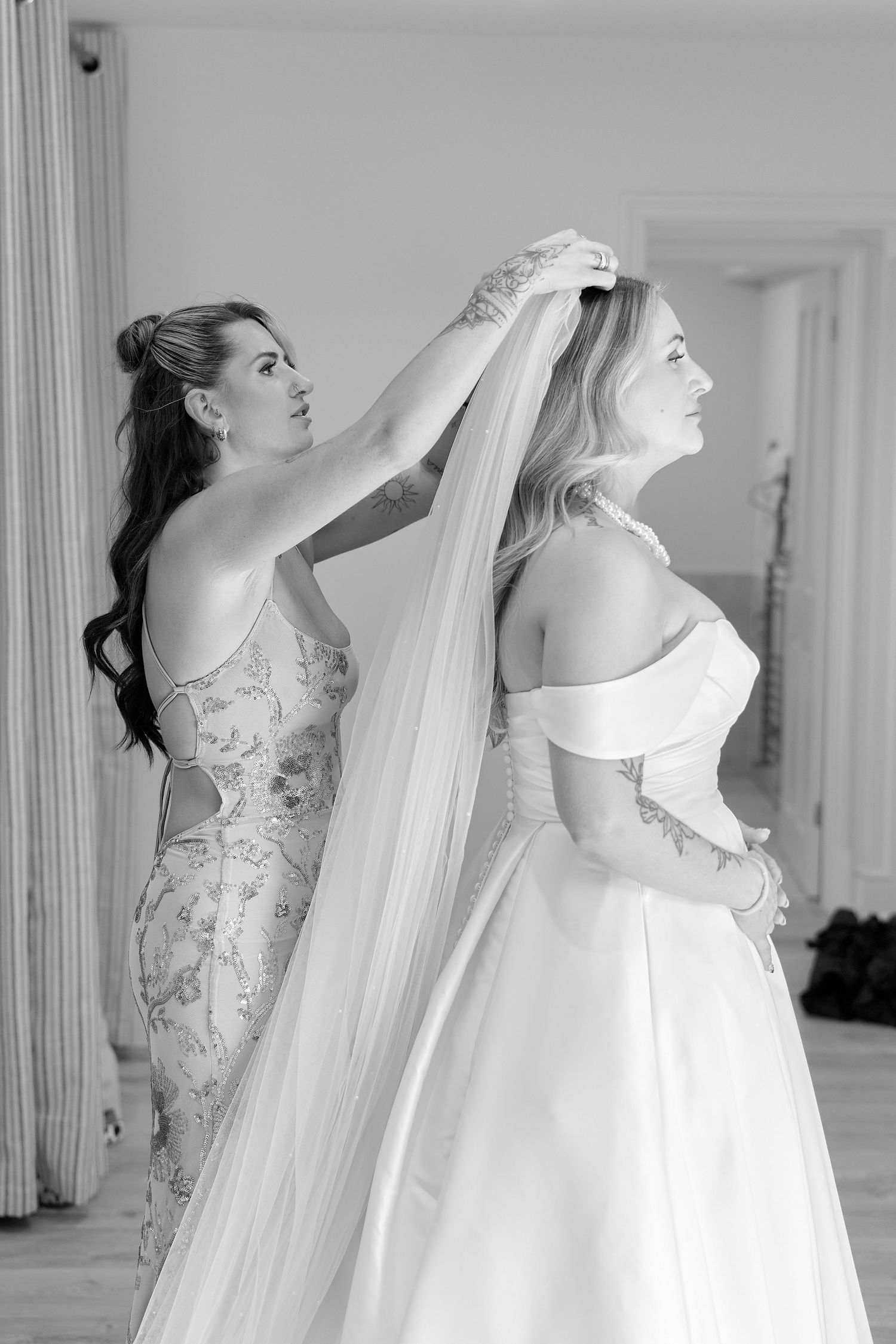 Bridesmaid helping bride with veil in elegant black and white wedding preparation photo.