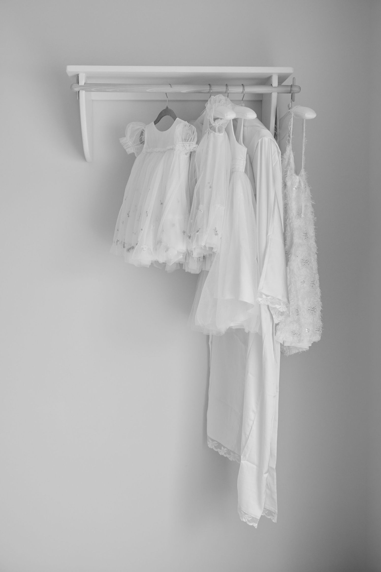 White lace dresses and bridal gown hanging on a wall-mounted rack, black and white photography.