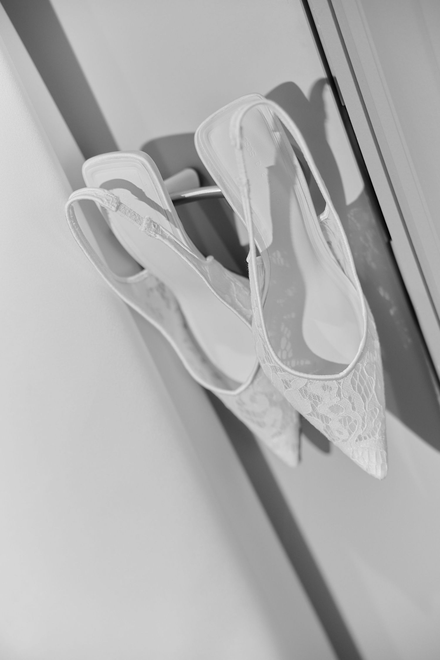 Black and white photo of elegant lace bridal slingback heels hanging on a wardrobe door.