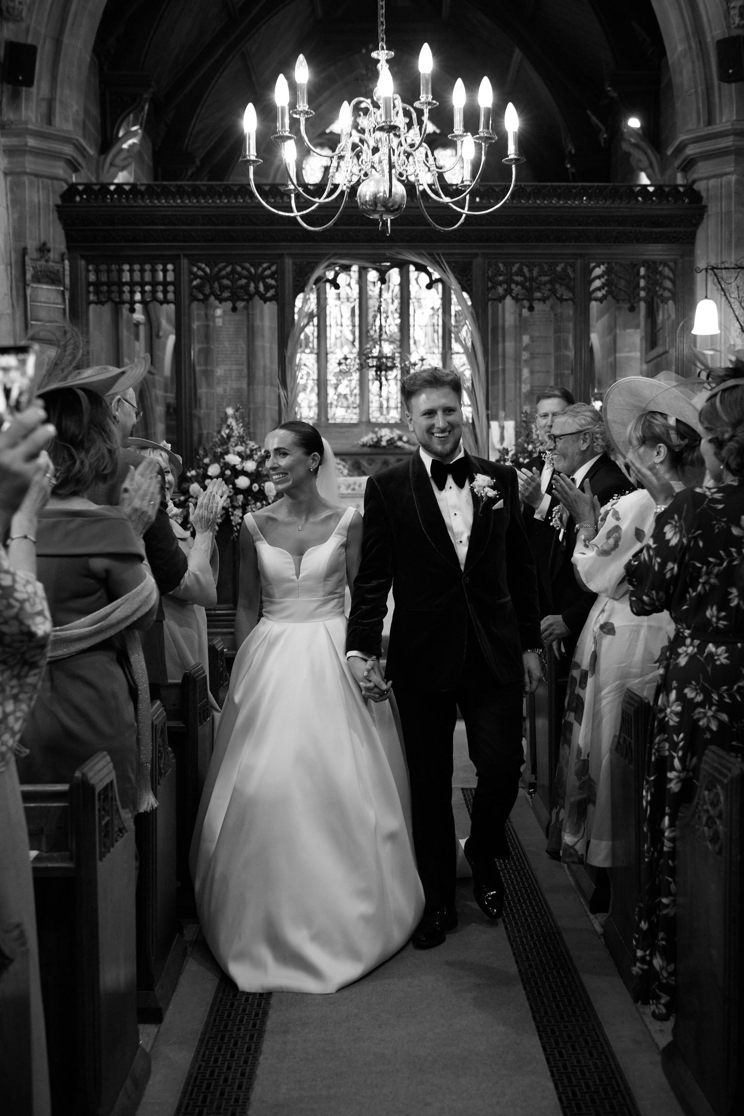 Black and white photo of a bride and groom walking down the aisle of a church after their wedding ceremony.