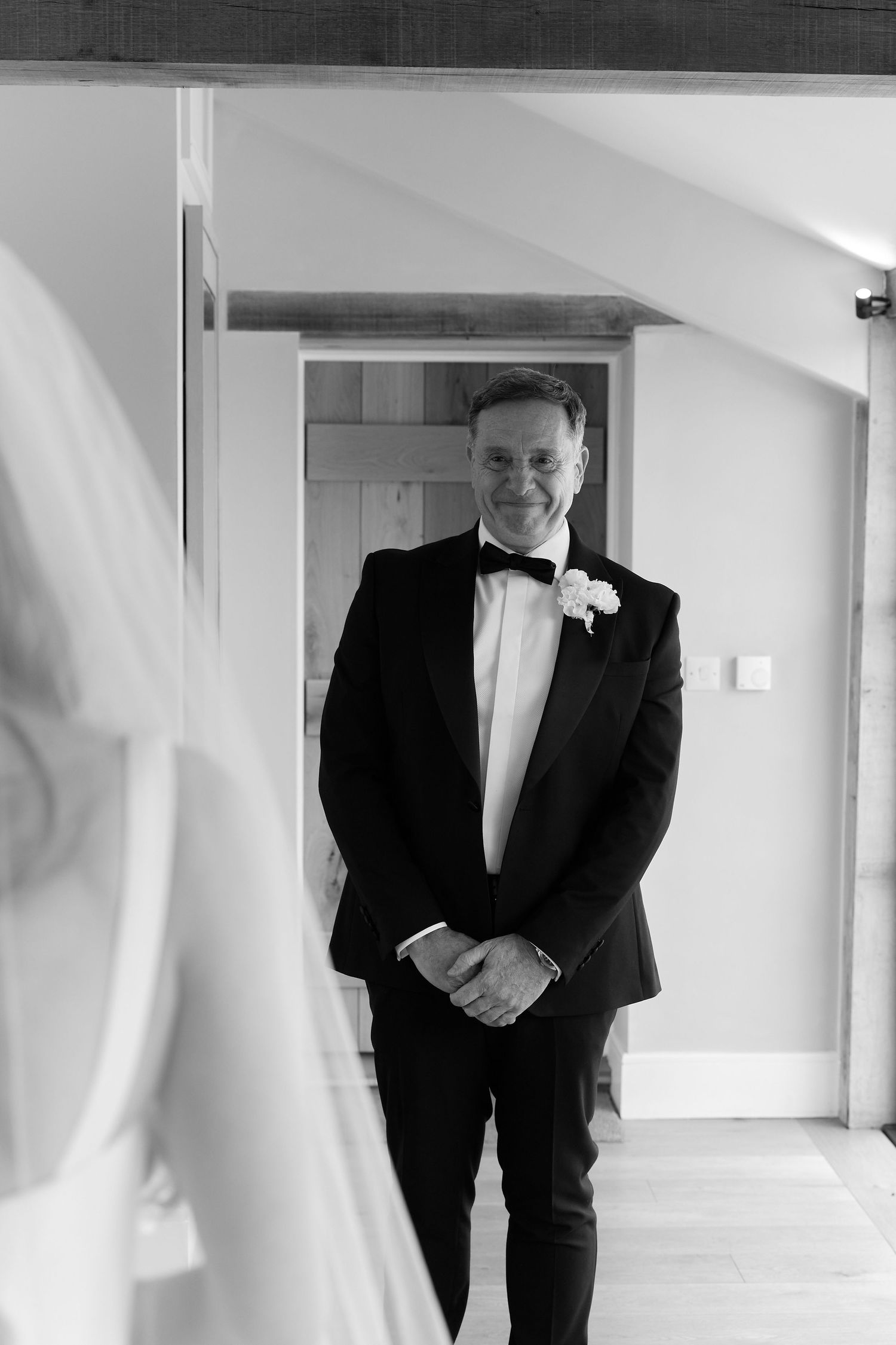 Groom in black tuxedo smiling as he sees bride for the first time, captured in elegant black and white.
