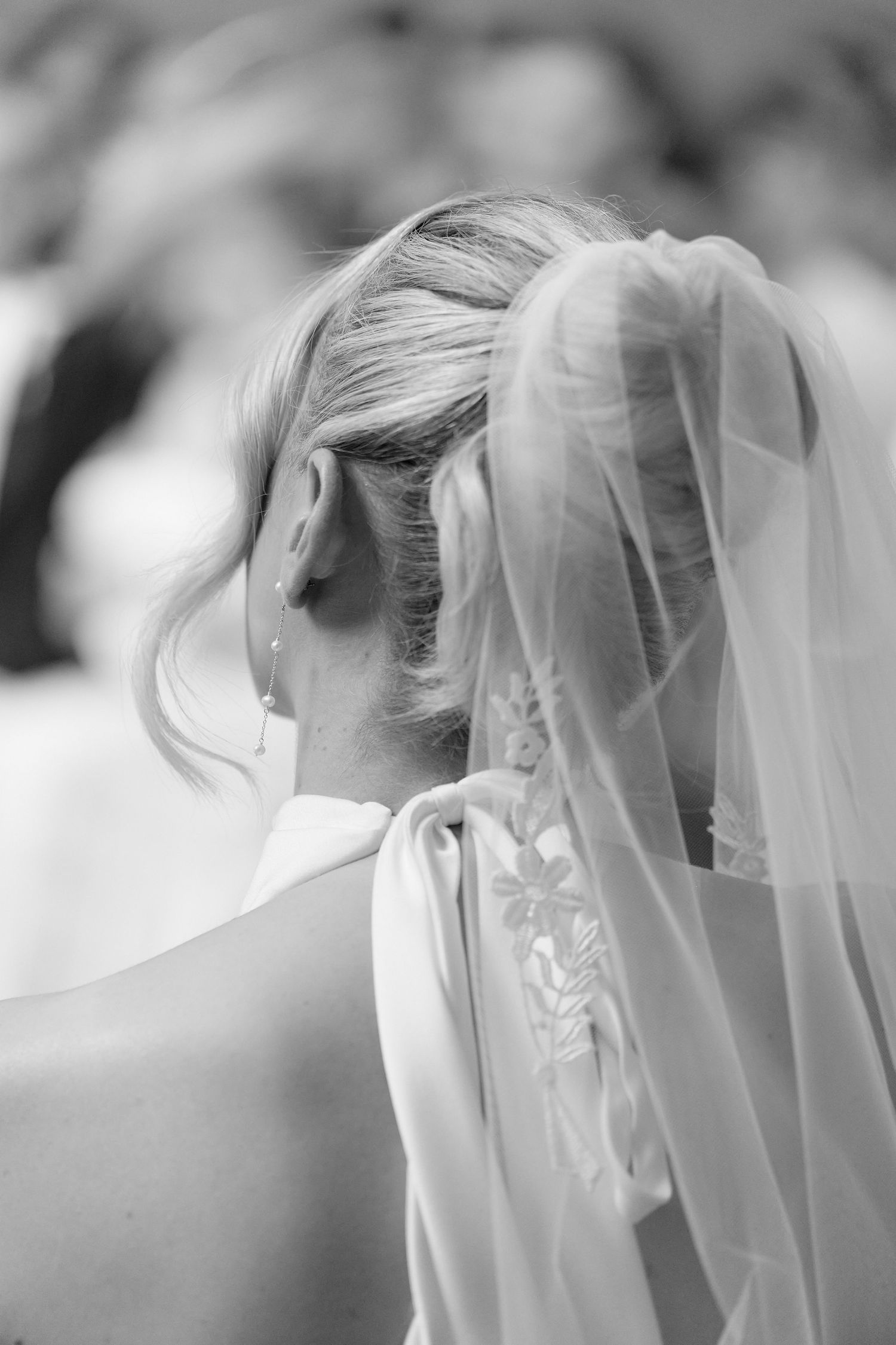 Close-up black and white detail of brides updo hairstyle and flowing veil from behind.