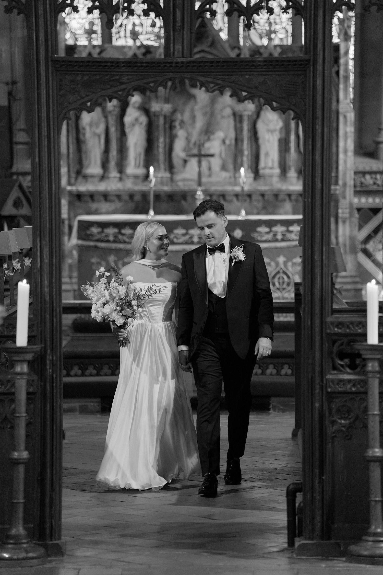 Black and white photo of a bride and groom walking through ornate church doors after their wedding ceremony.