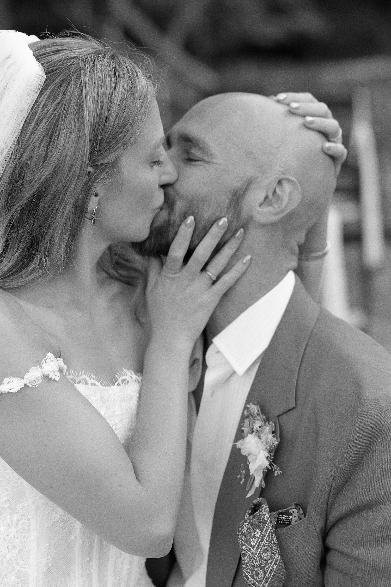 Black and white photo of a bride and groom sharing a kiss on their wedding day, bride in lace dress.