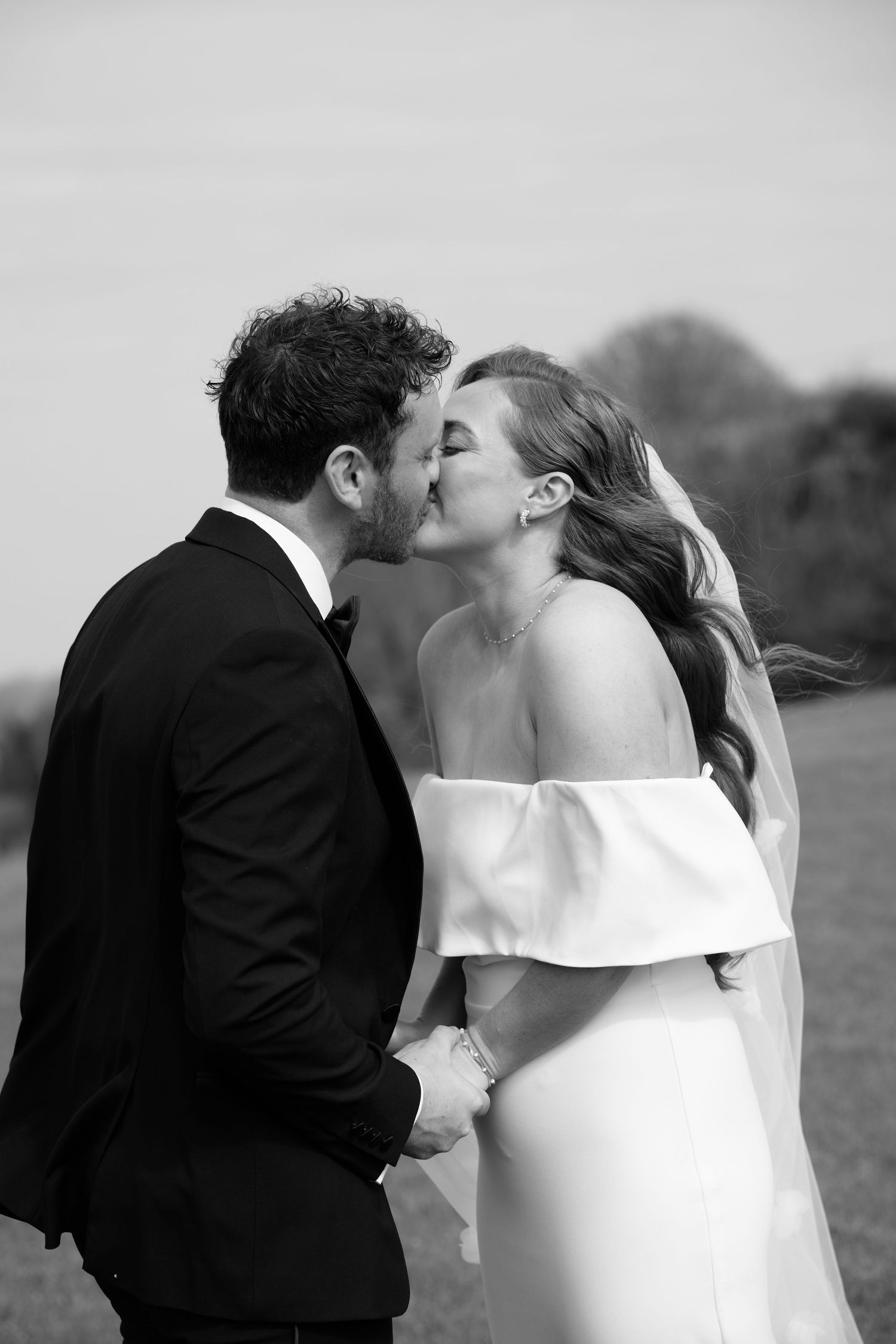 Black and white photo of a bride and groom sharing a romantic kiss outdoors on their wedding day.