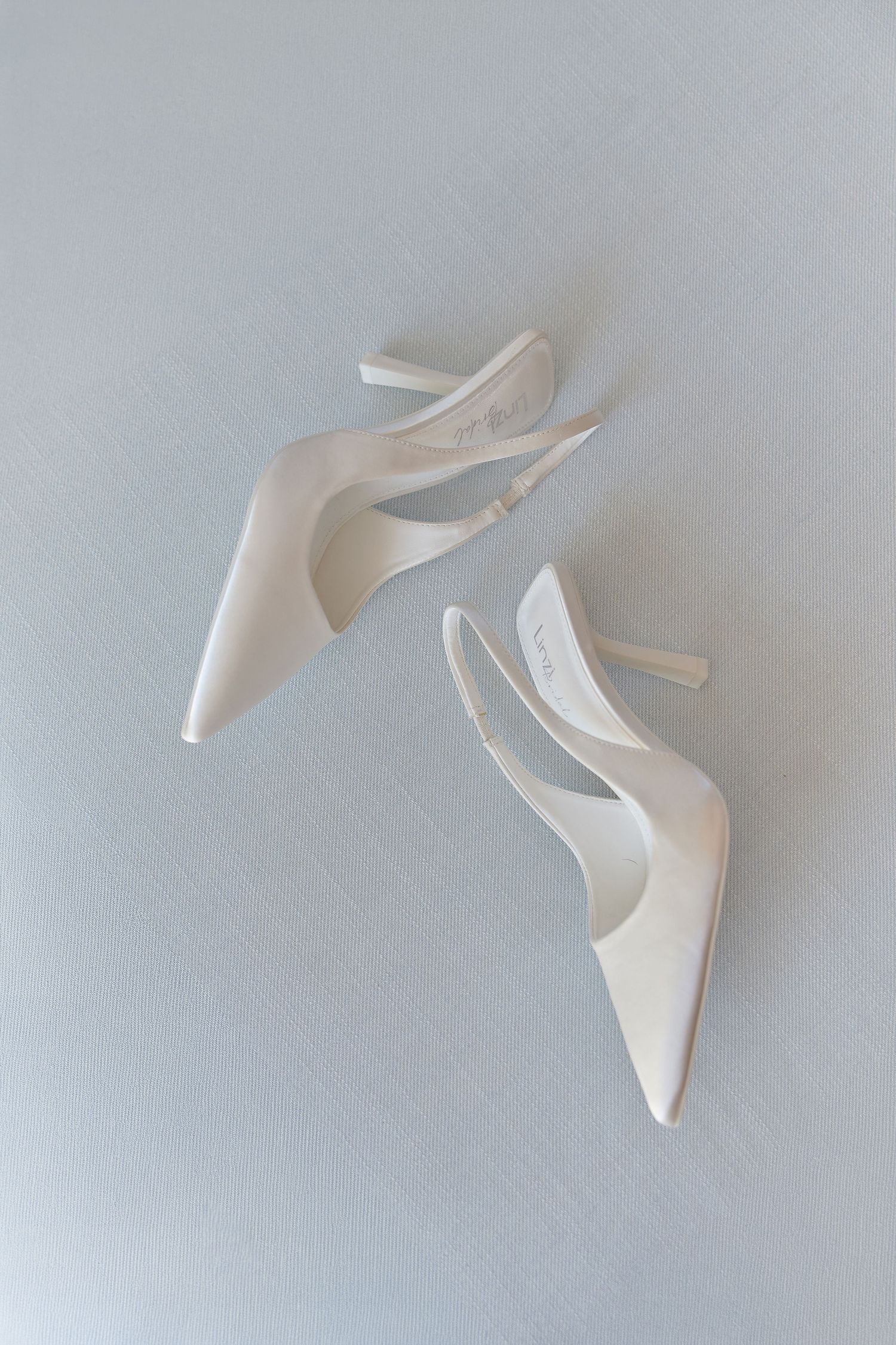 Elegant white satin slingback stiletto heels displayed on a light gray surface, perfect for bridal or formal occasions.
