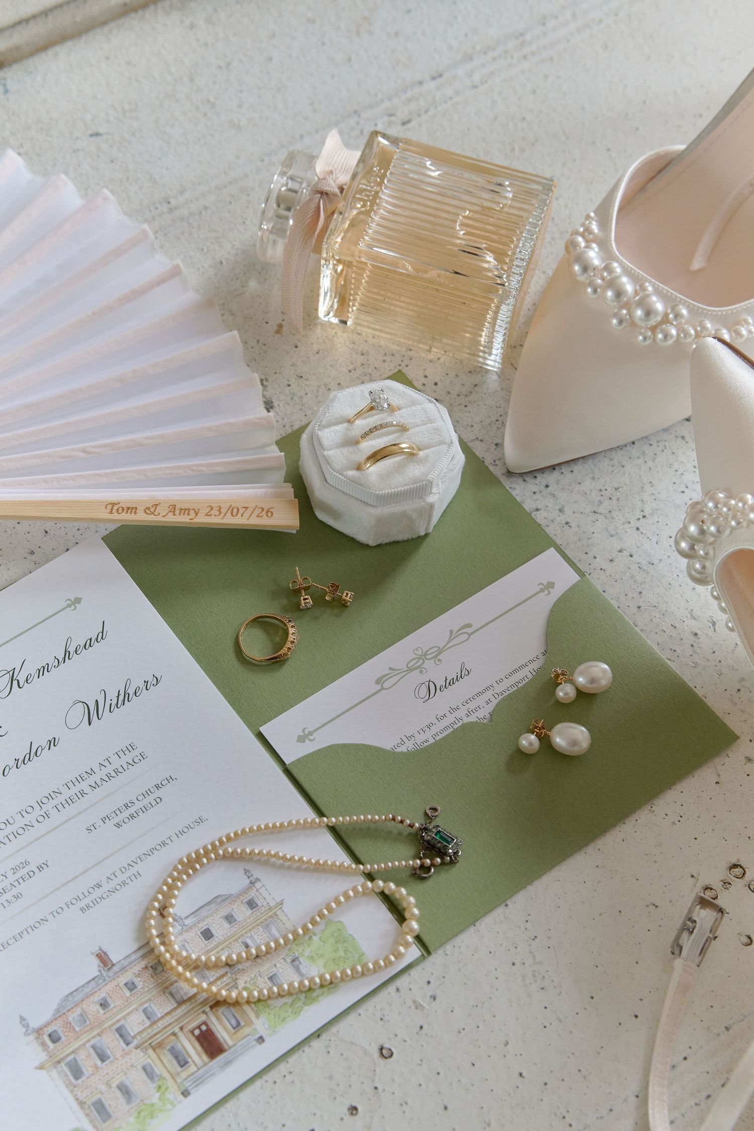 Elegant bridal flat lay featuring pearl jewelry, gold rings, wedding invitation, perfume bottle, and pearl-embellished heels.
