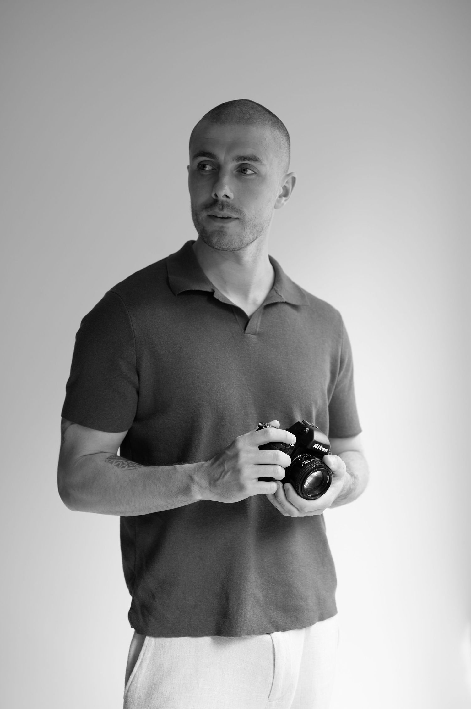 Man holding Nikon camera in black and white studio portrait wearing polo shirt.